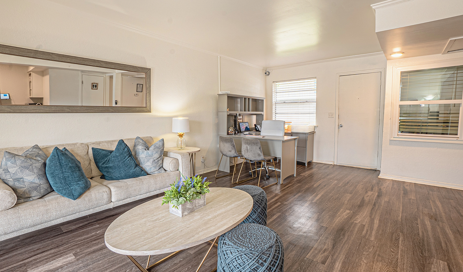 Bright and inviting living room with modern decor, featuring a cozy sofa with plush pillows, a stylish coffee table, and a functional desk space near large windows.