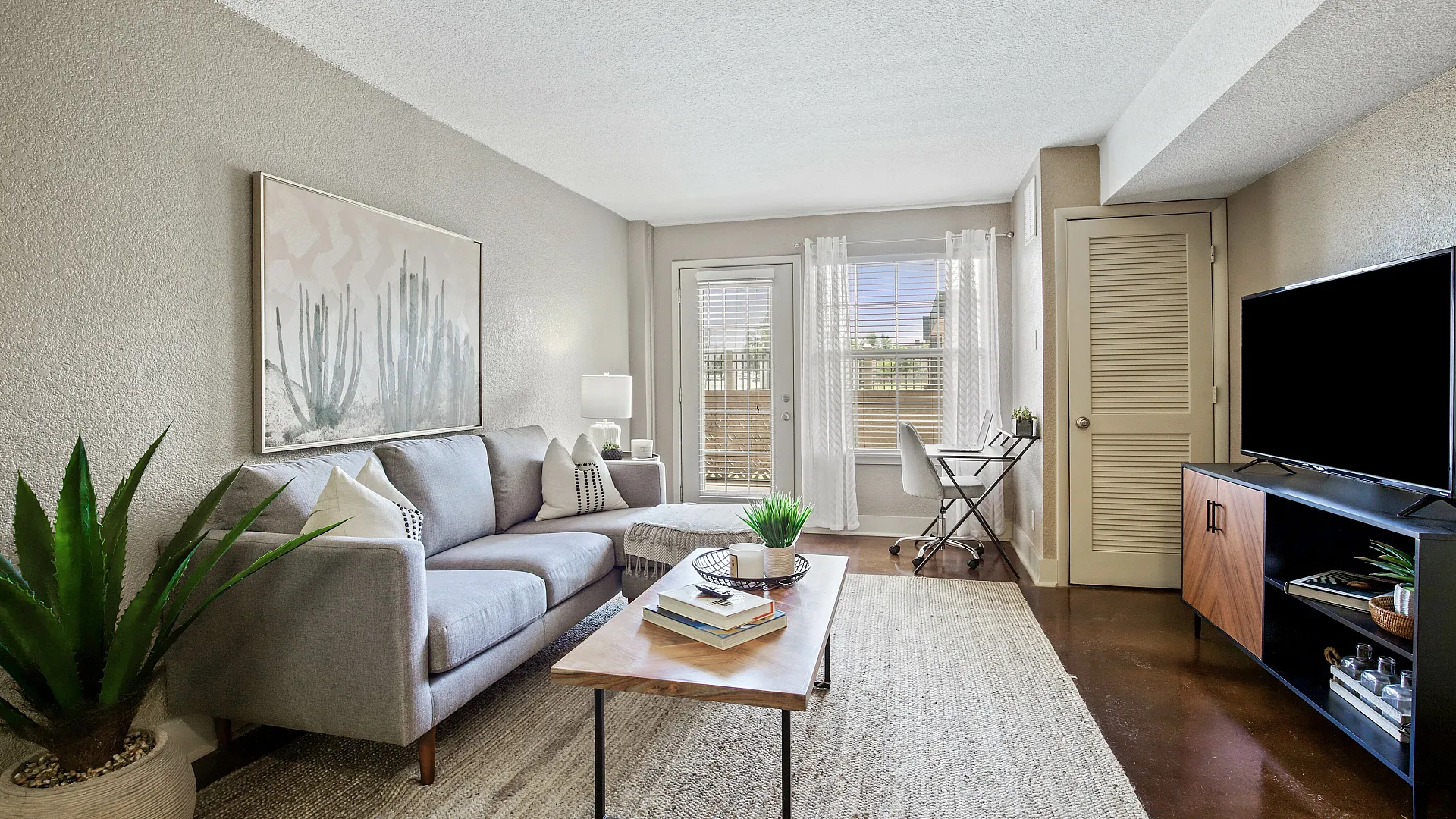 Inviting living room with a modern gray sofa, chic decor, and natural light streaming through large windows, creating a cozy workspace nook.