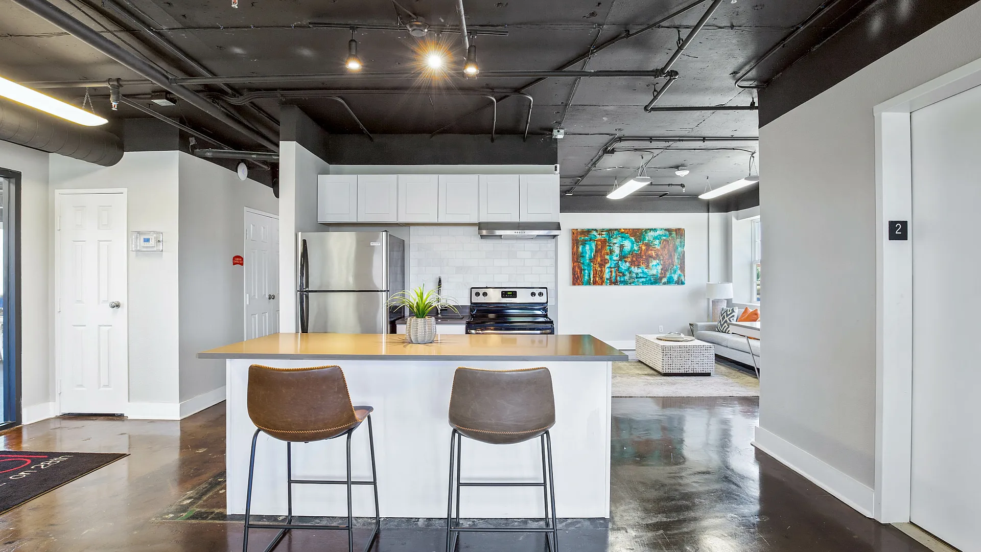 Modern open-concept apartment kitchen with sleek stainless steel appliances, chic island seating, and a stylish living room in the background.