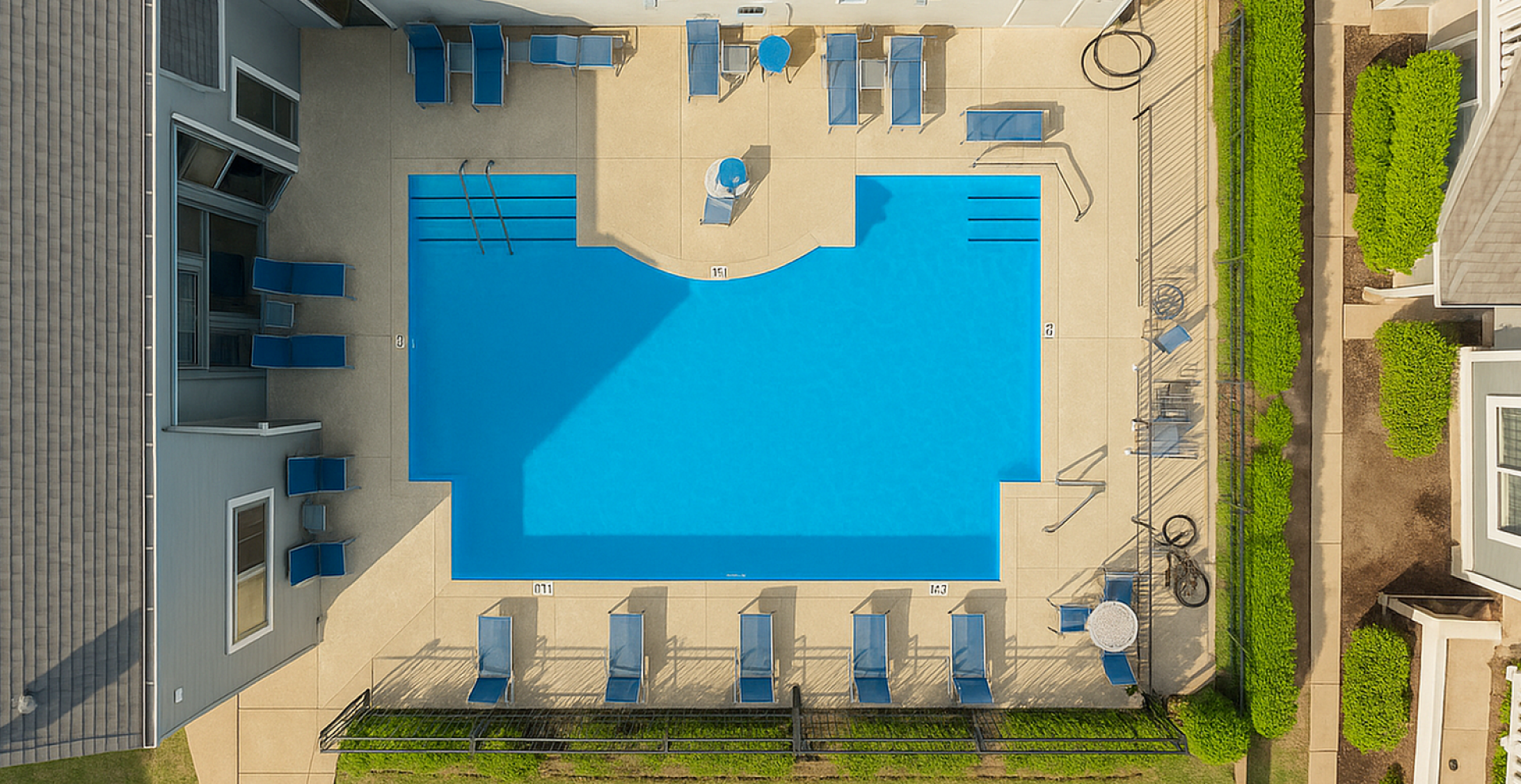 Aerial view of a luxurious apartment complex pool area, featuring a pristine blue swimming pool surrounded by comfortable lounge chairs and vibrant greenery.
