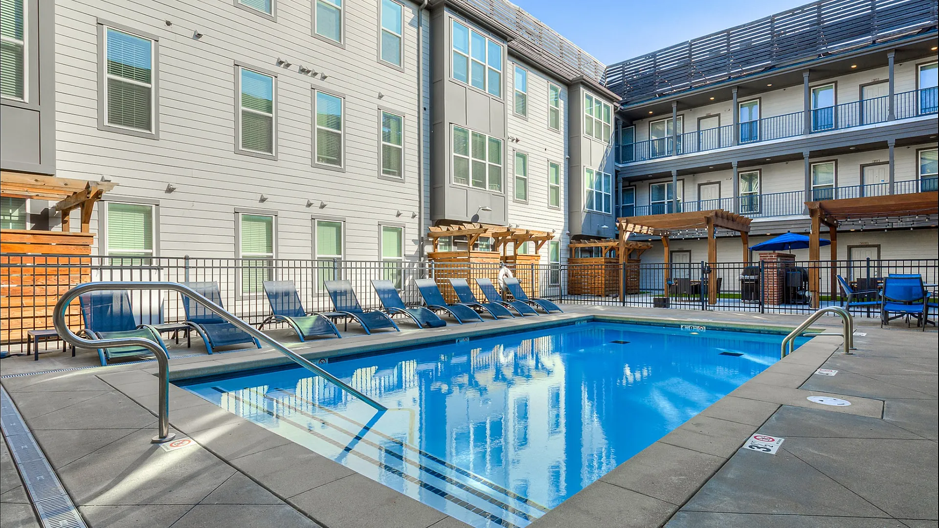 Modern apartment complex courtyard with a sparkling swimming pool surrounded by stylish lounge chairs and elegant pergolas.