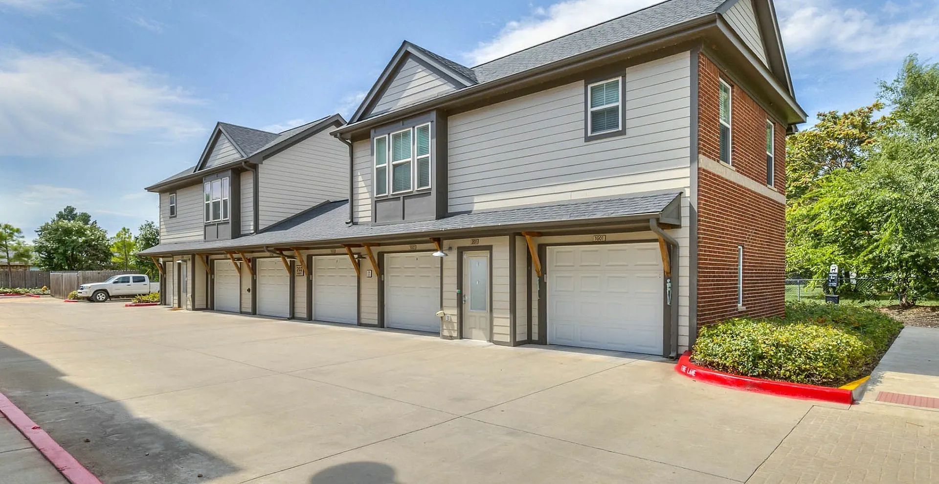 Modern two-story townhouse with private garages, attractive brick and siding exterior, surrounded by lush greenery under a clear sky.