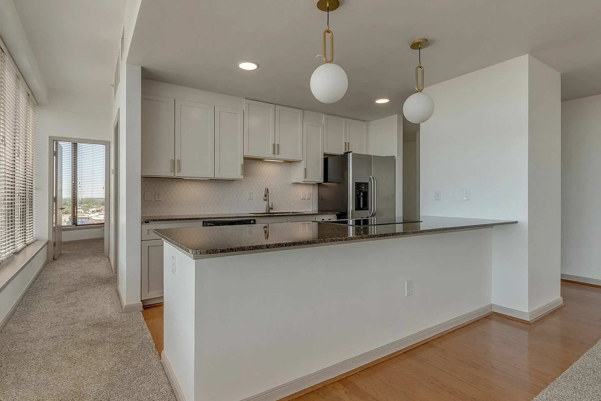 Modern kitchen with sleek granite countertops, chic pendant lighting, and stainless steel appliances in a bright, open-concept apartment.