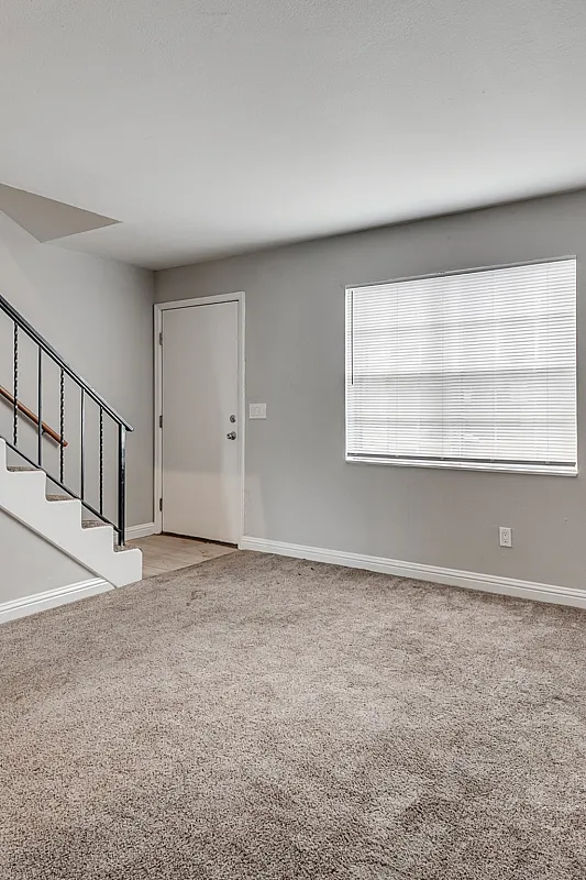 Bright and inviting living space featuring plush carpet, modern railing staircase, and ample natural light from large window.