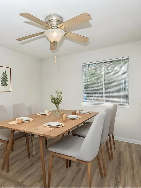 Elegant dining room with a wooden table set for six, modern decor, and natural light through a large window.