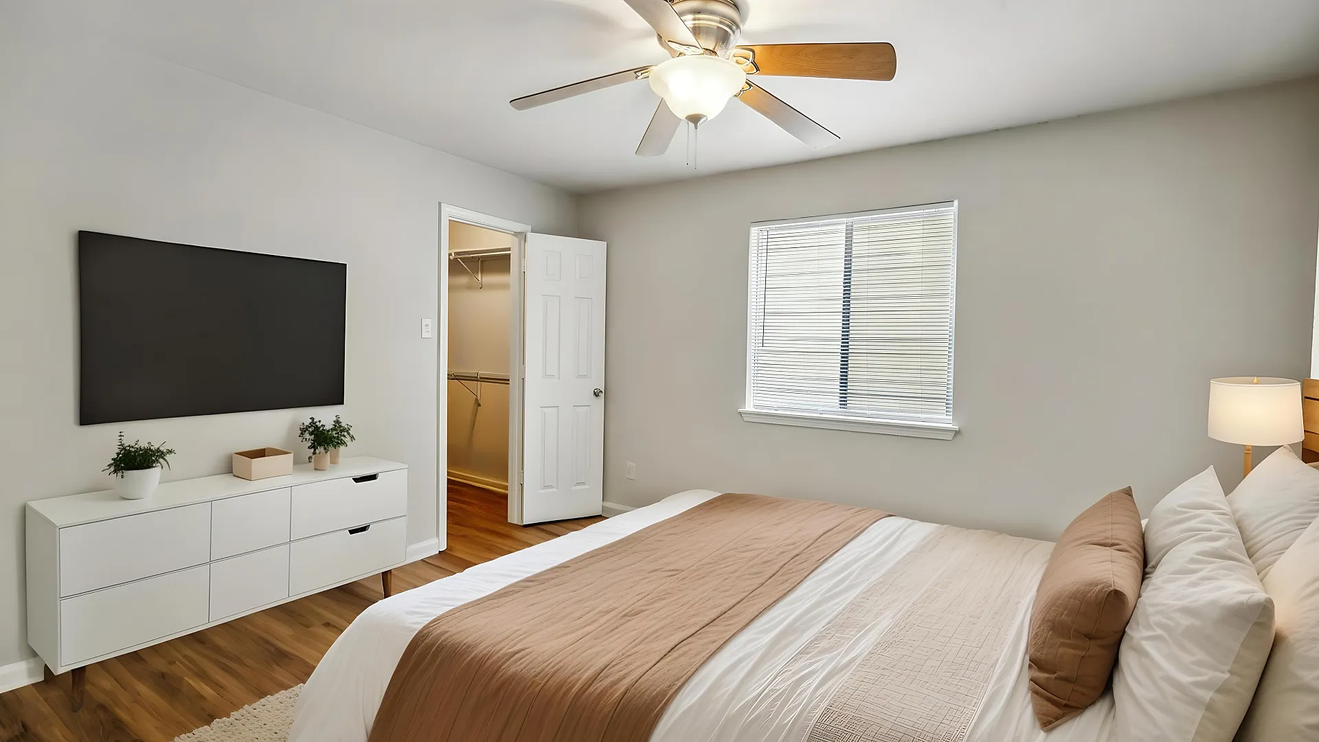 Inviting bedroom with modern ceiling fan, cozy bed setup, and elegant wooden flooring, featuring a spacious walk-in closet and ample natural light.