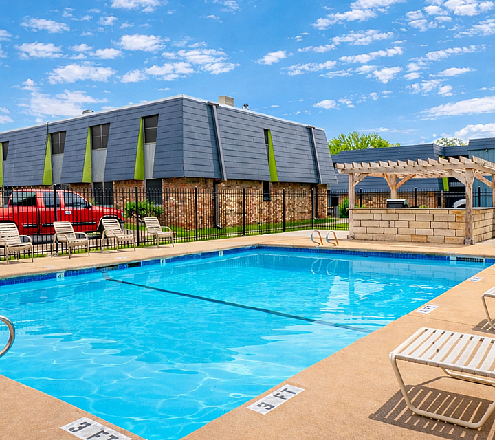 Inviting apartment pool area with sun loungers, vibrant blue skies, and a charming pergola, perfect for relaxation.