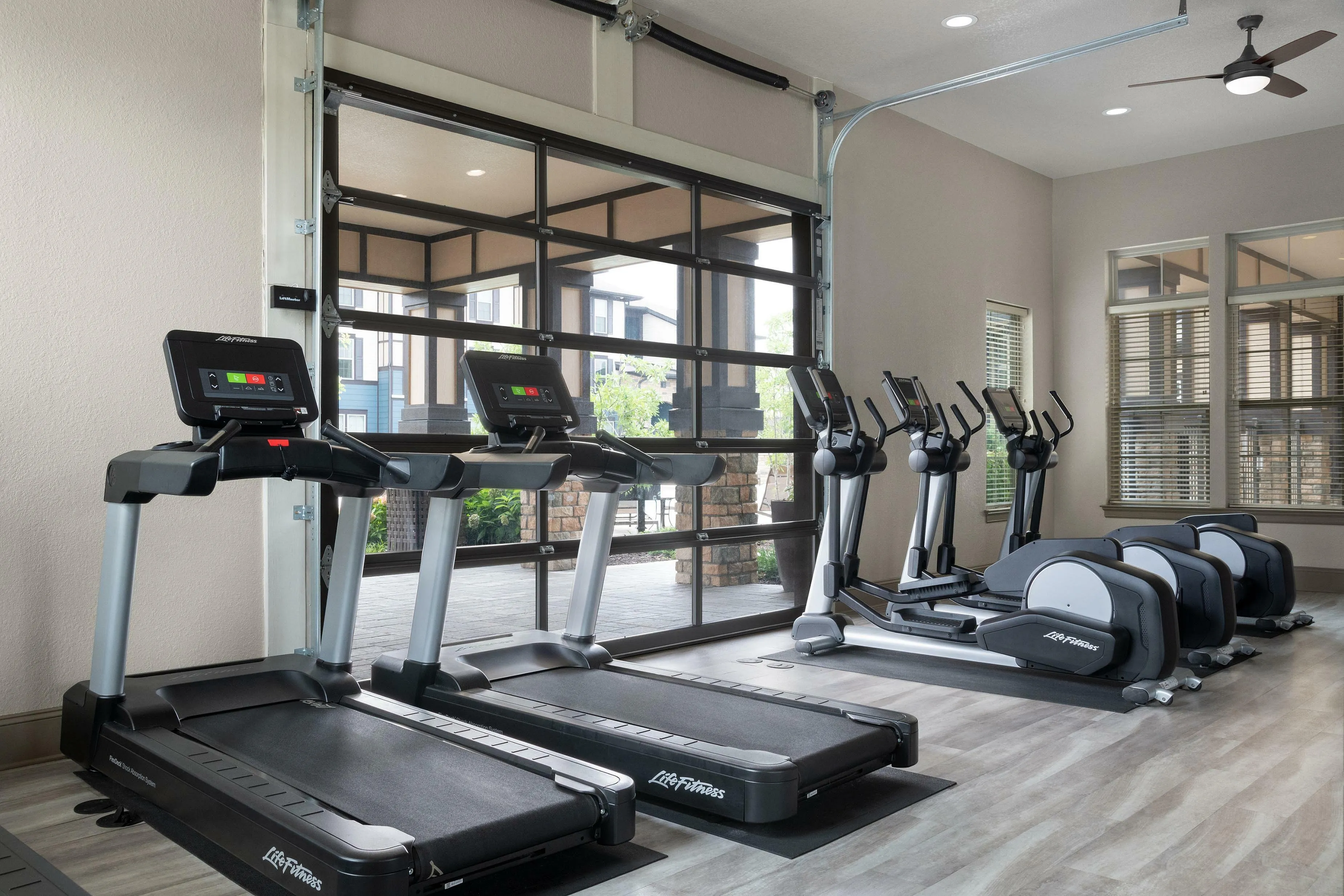 Modern fitness center with treadmills and ellipticals in a bright, spacious room with large windows.