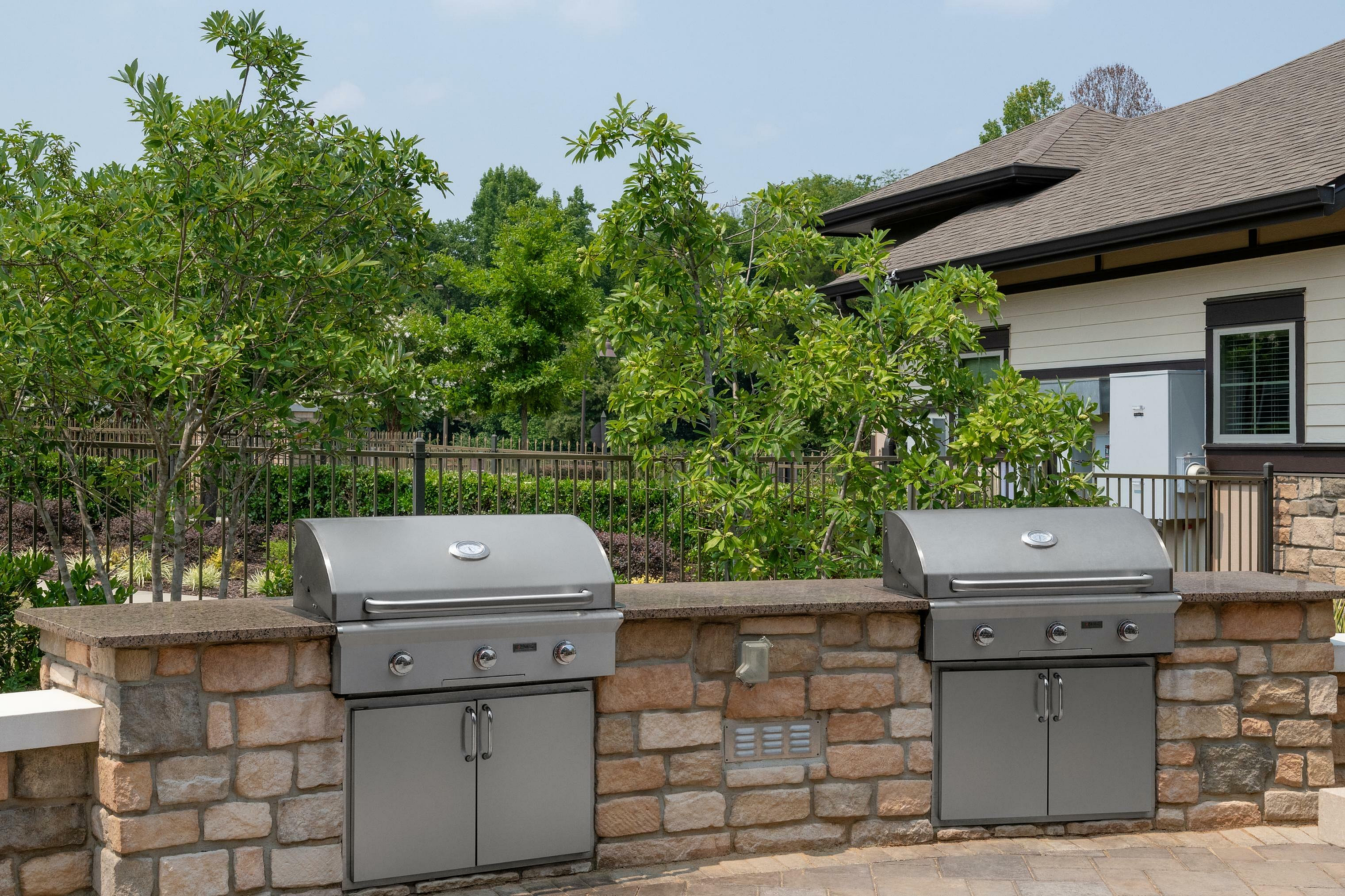 Elegant outdoor grilling area with two modern stainless steel grills and lush green surroundings.
