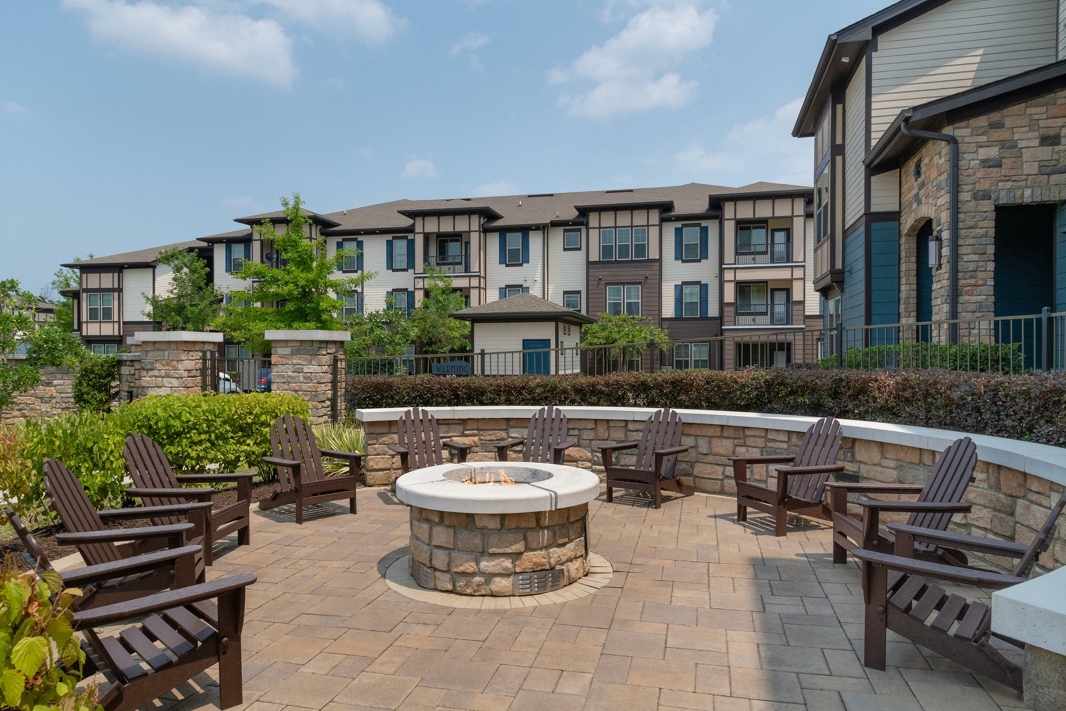 Inviting outdoor patio area with a central fire pit surrounded by Adirondack chairs in front of modern apartment complex.