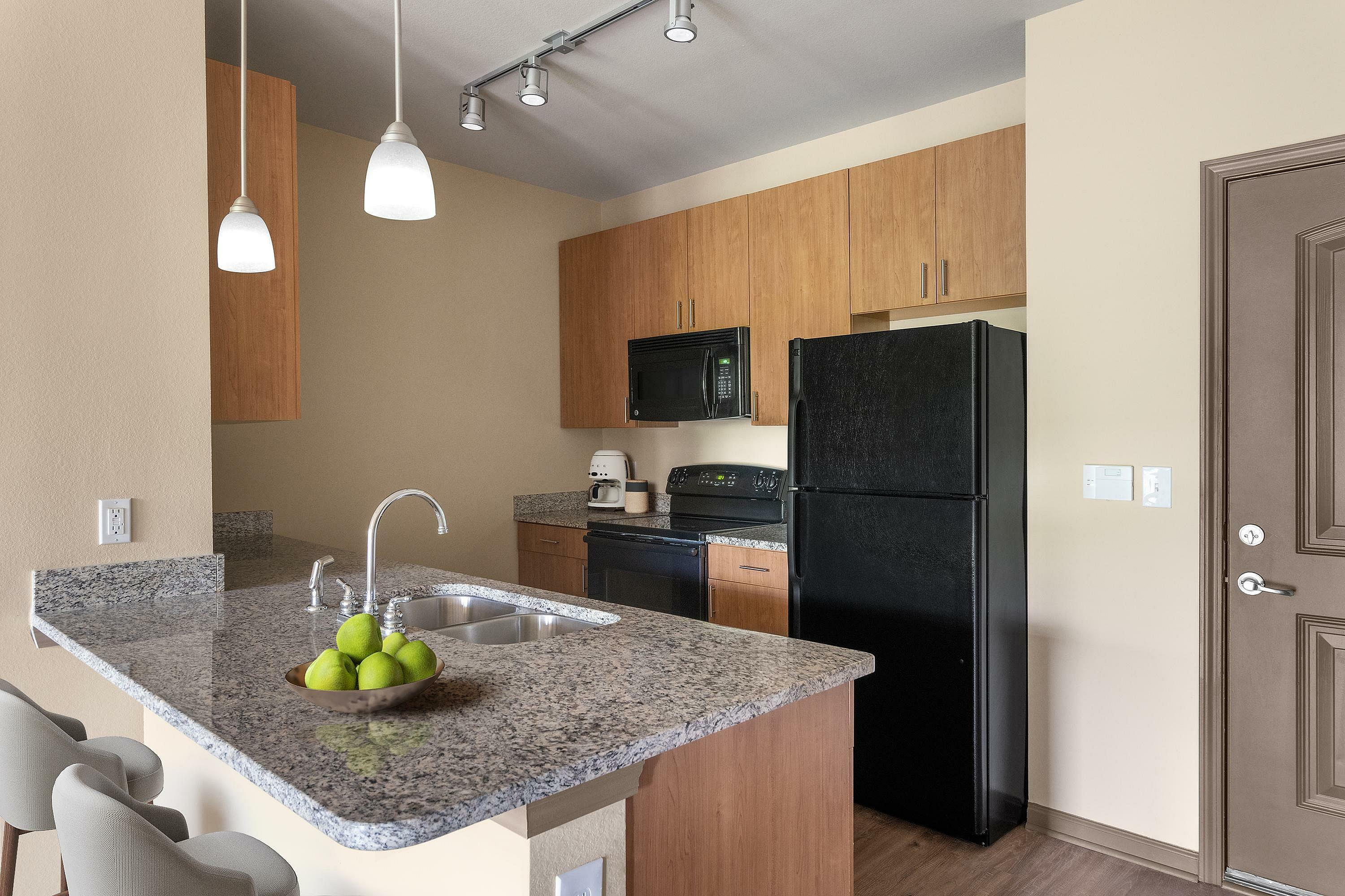 Modern kitchen with sleek granite countertops, stylish lighting, and warm wood cabinetry.