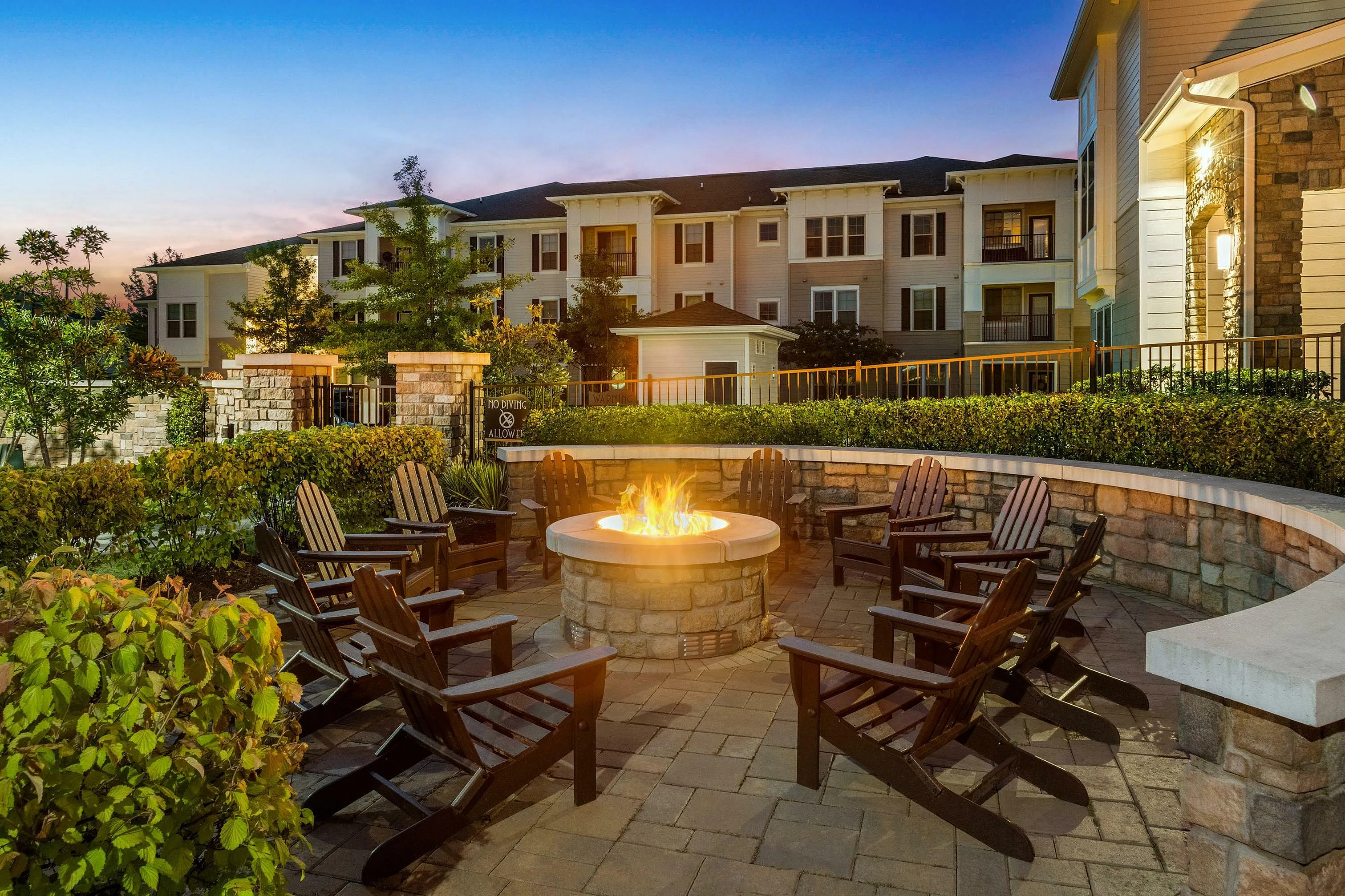 Inviting outdoor seating area with a warm fire pit surrounded by lush greenery at sunset.
