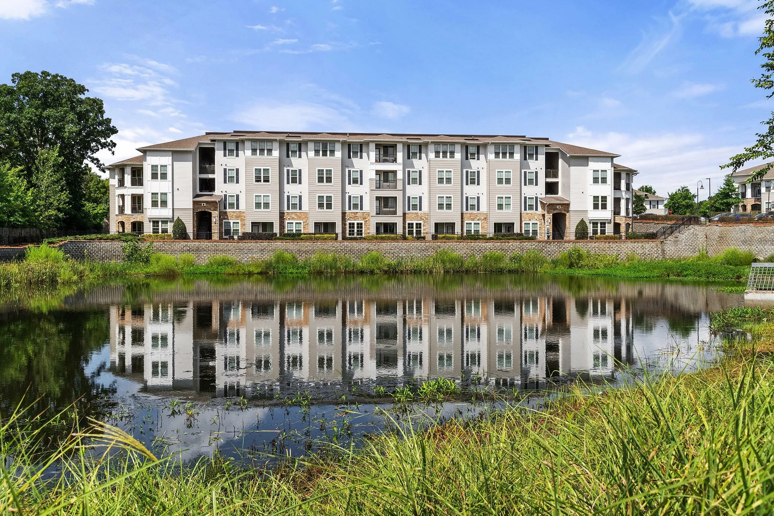 Elegant four-story apartment complex with a reflective lake and lush greenery.