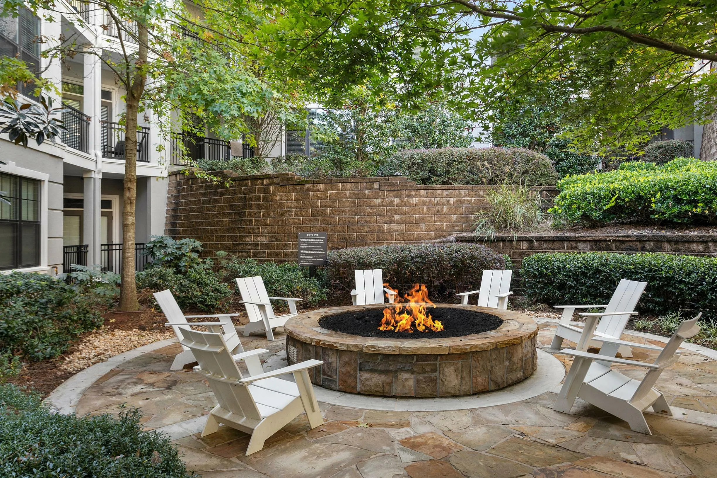 Charming outdoor fire pit surrounded by Adirondack chairs amidst lush greenery.