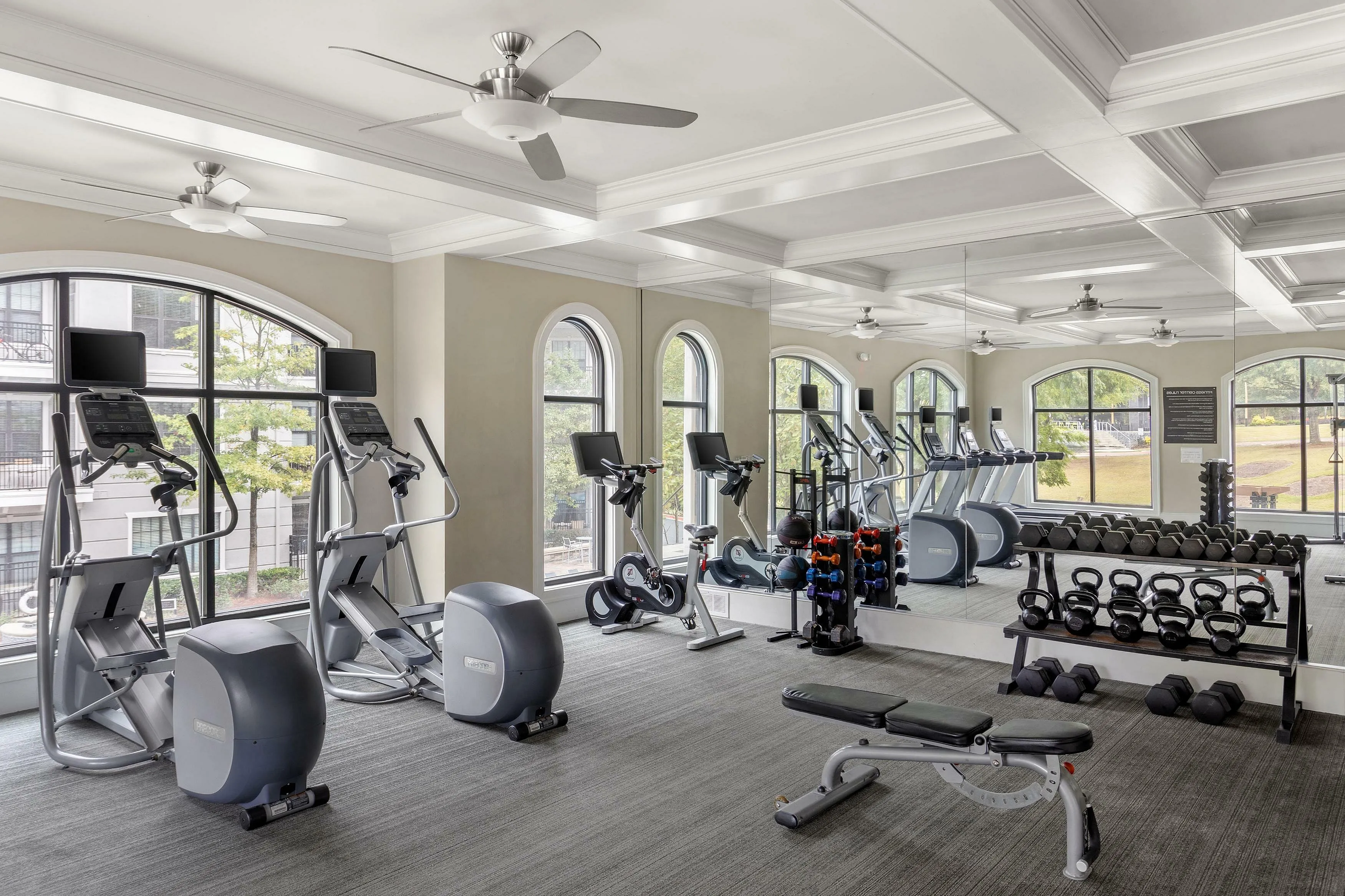 Spacious and modern apartment gym with cardio machines, free weights, and mirrored walls.