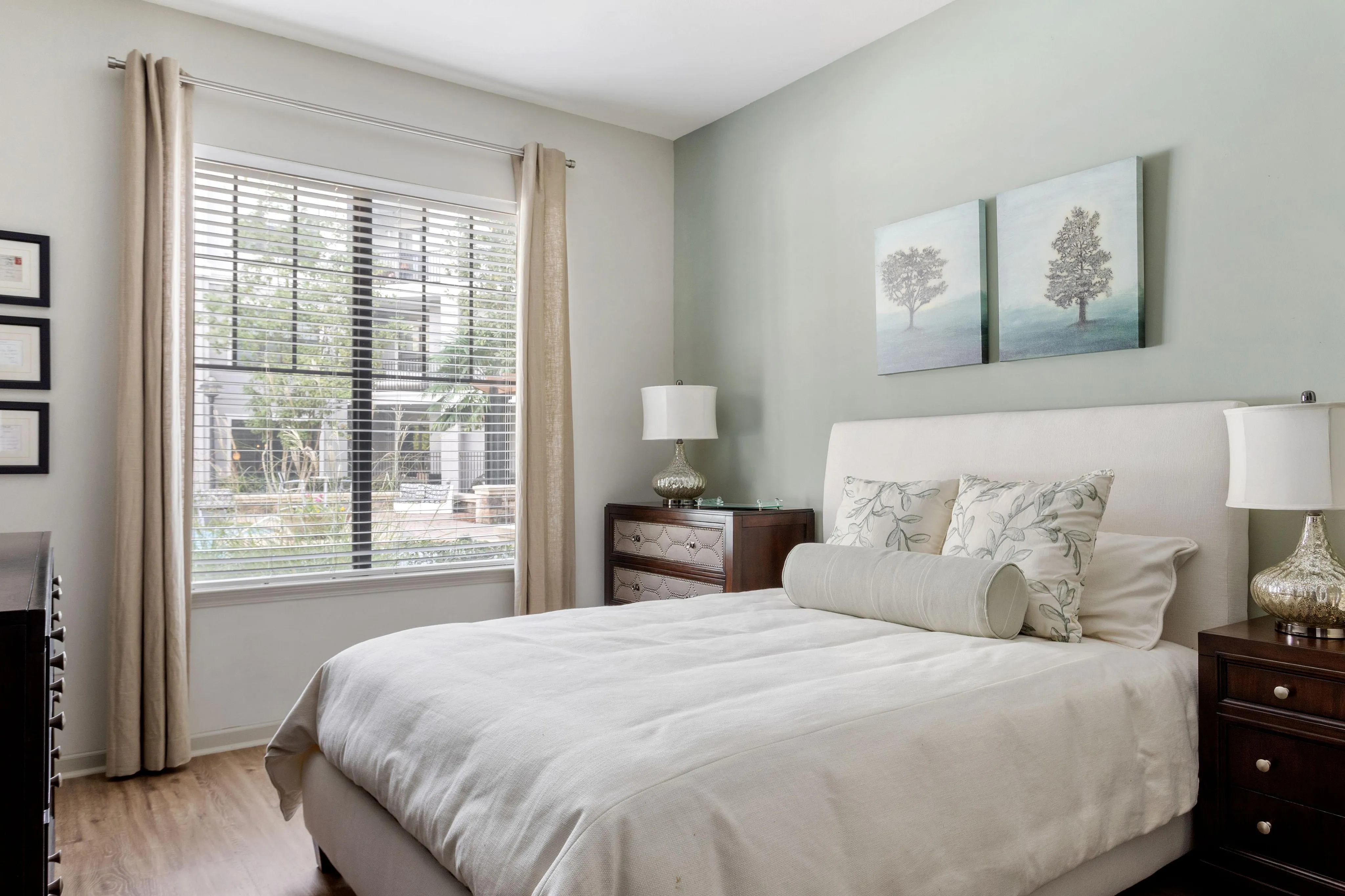 Bright and airy bedroom with soft color scheme, featuring a comfortable bed, decorative pillows, elegant curtains, and nature-inspired artwork.
