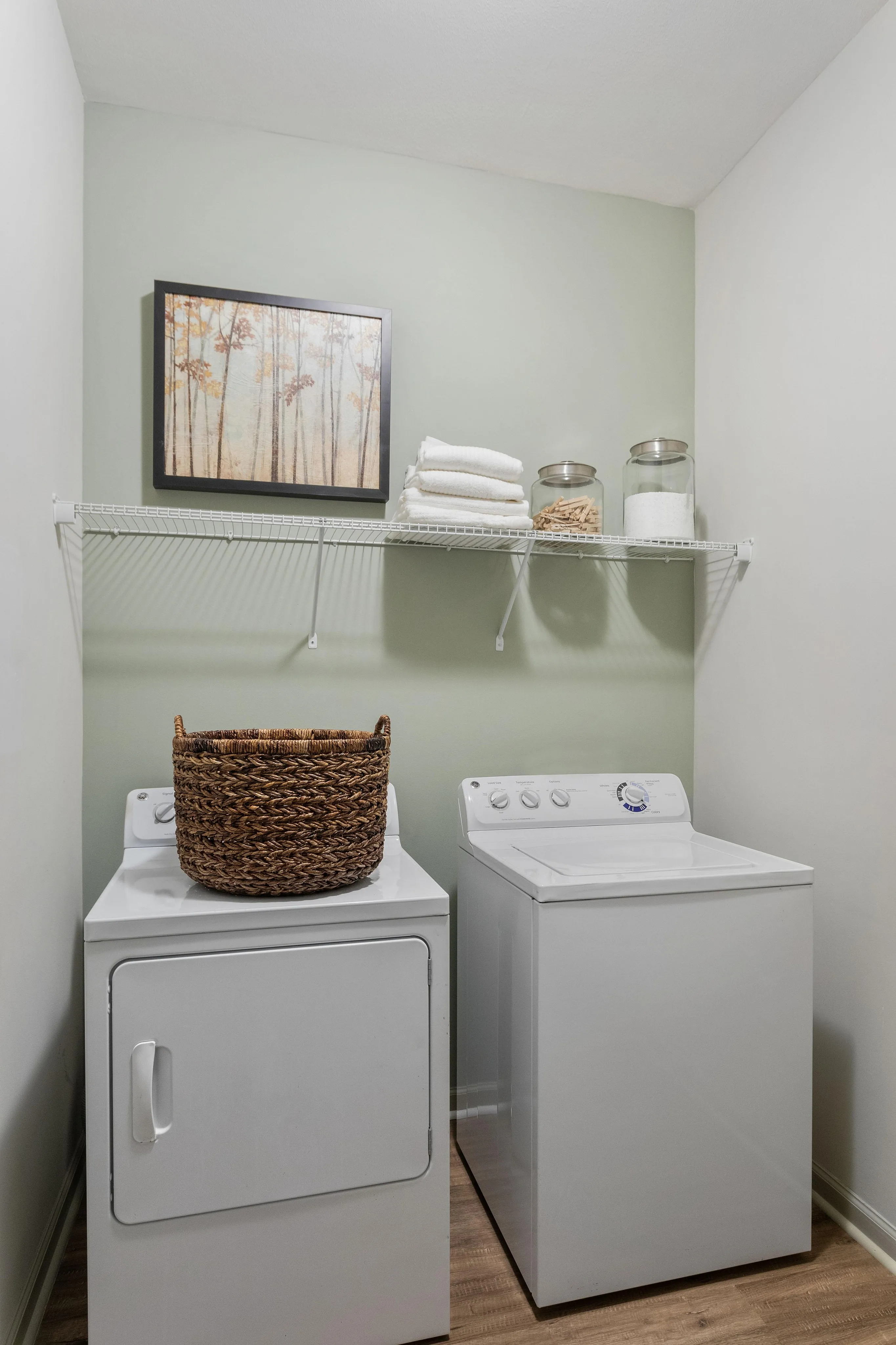 Inviting laundry room featuring a washer, dryer, wicker basket, and neatly arranged shelves with jars and towels.