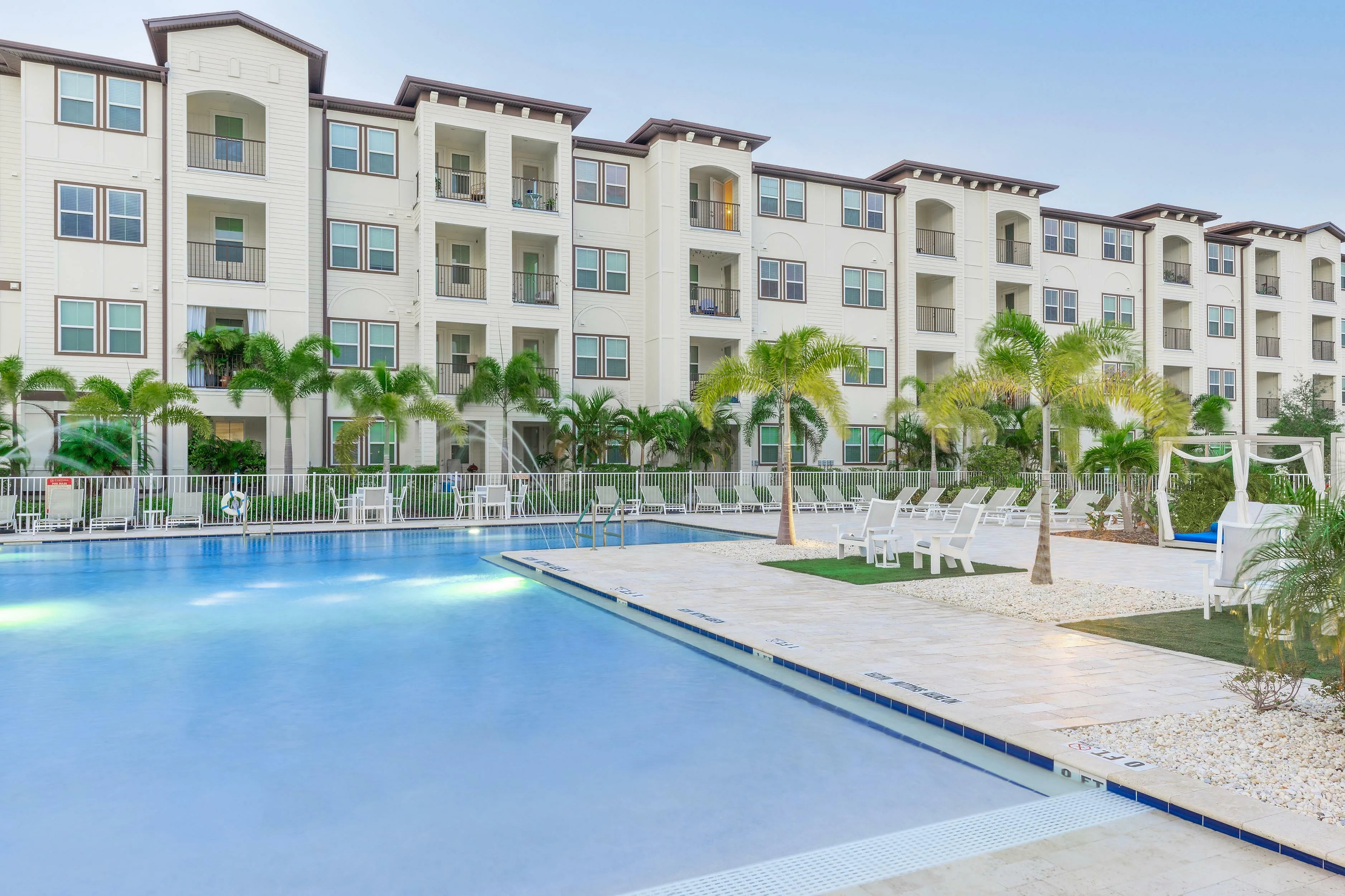Luxurious apartment complex with modern architecture and a serene poolside area surrounded by palm trees.
