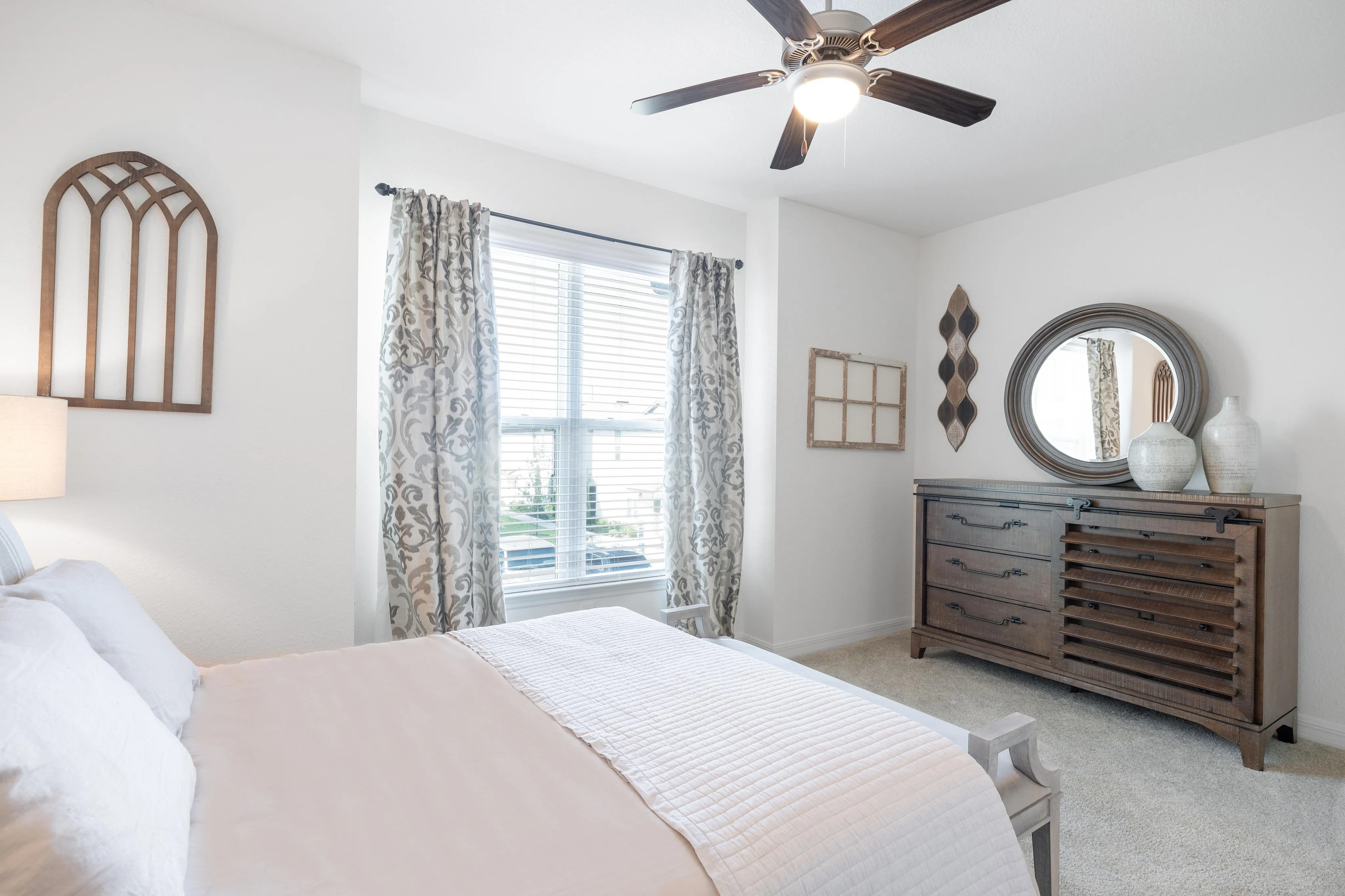 Bright and welcoming bedroom with a large window, stylish dresser, and decorative elements.