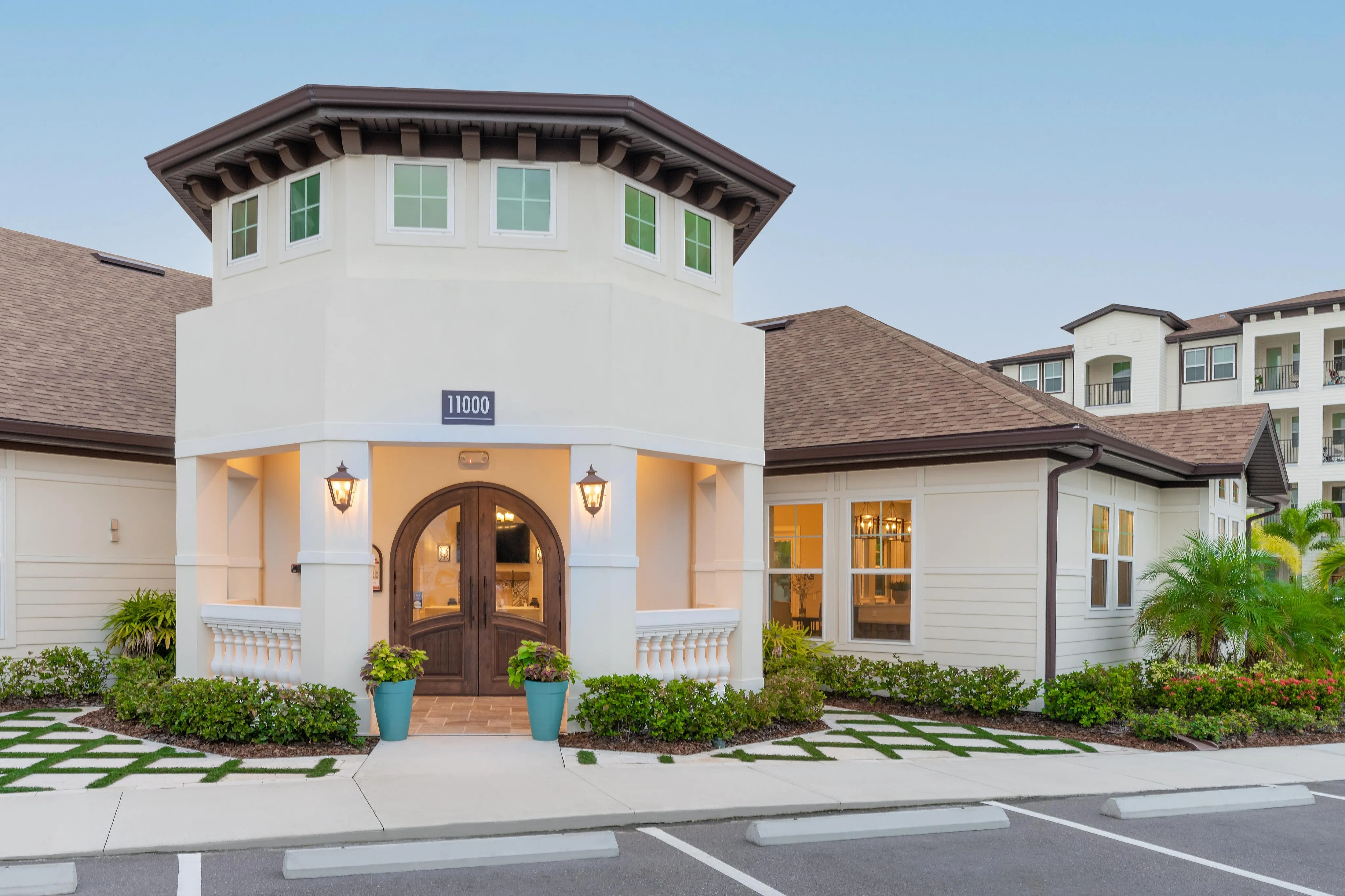 Stylish entrance of a modern apartment complex featuring a round doorway, lantern lights, and beautifully landscaped surroundings.