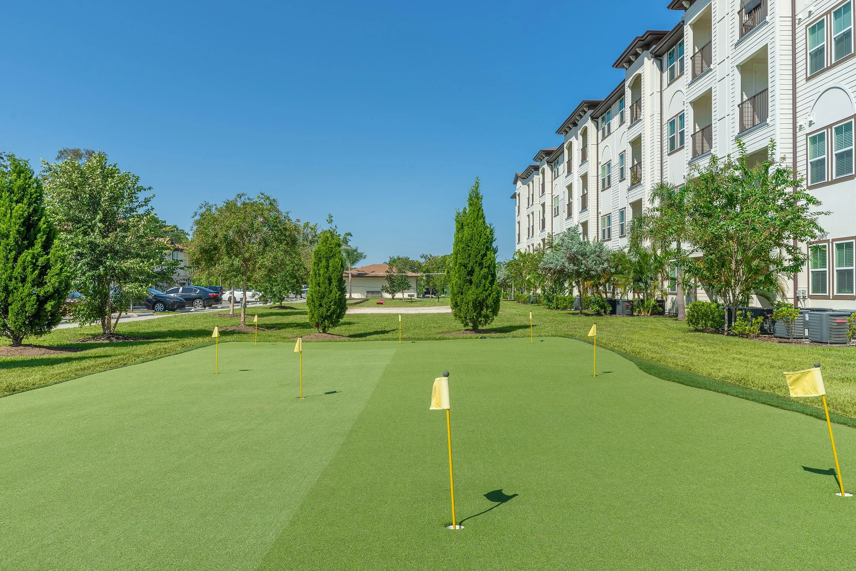 Beautiful outdoor putting green beside a modern apartment building with lush landscaping.