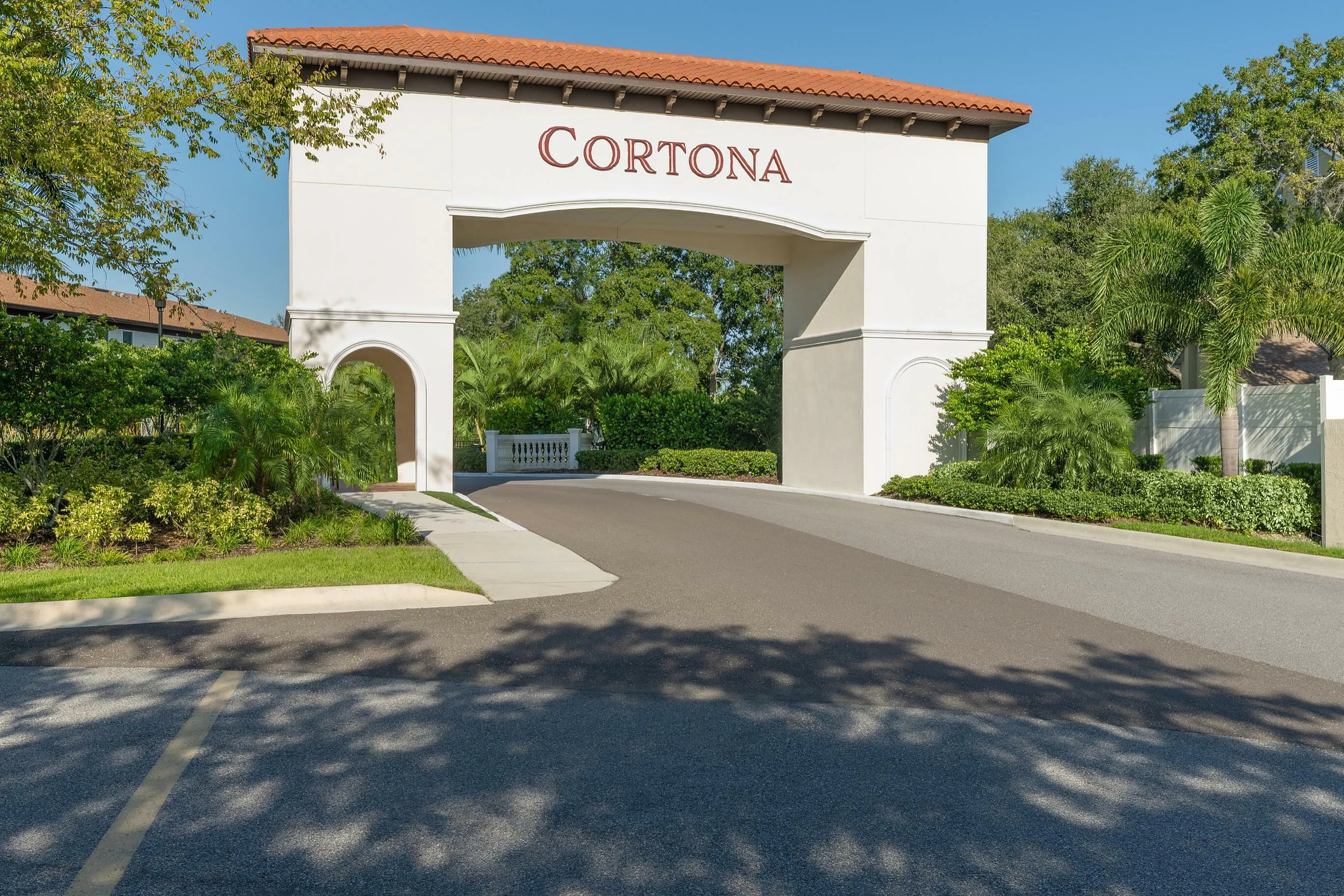 Elegant entrance archway at Cortona, surrounded by lush greenery under a clear blue sky.