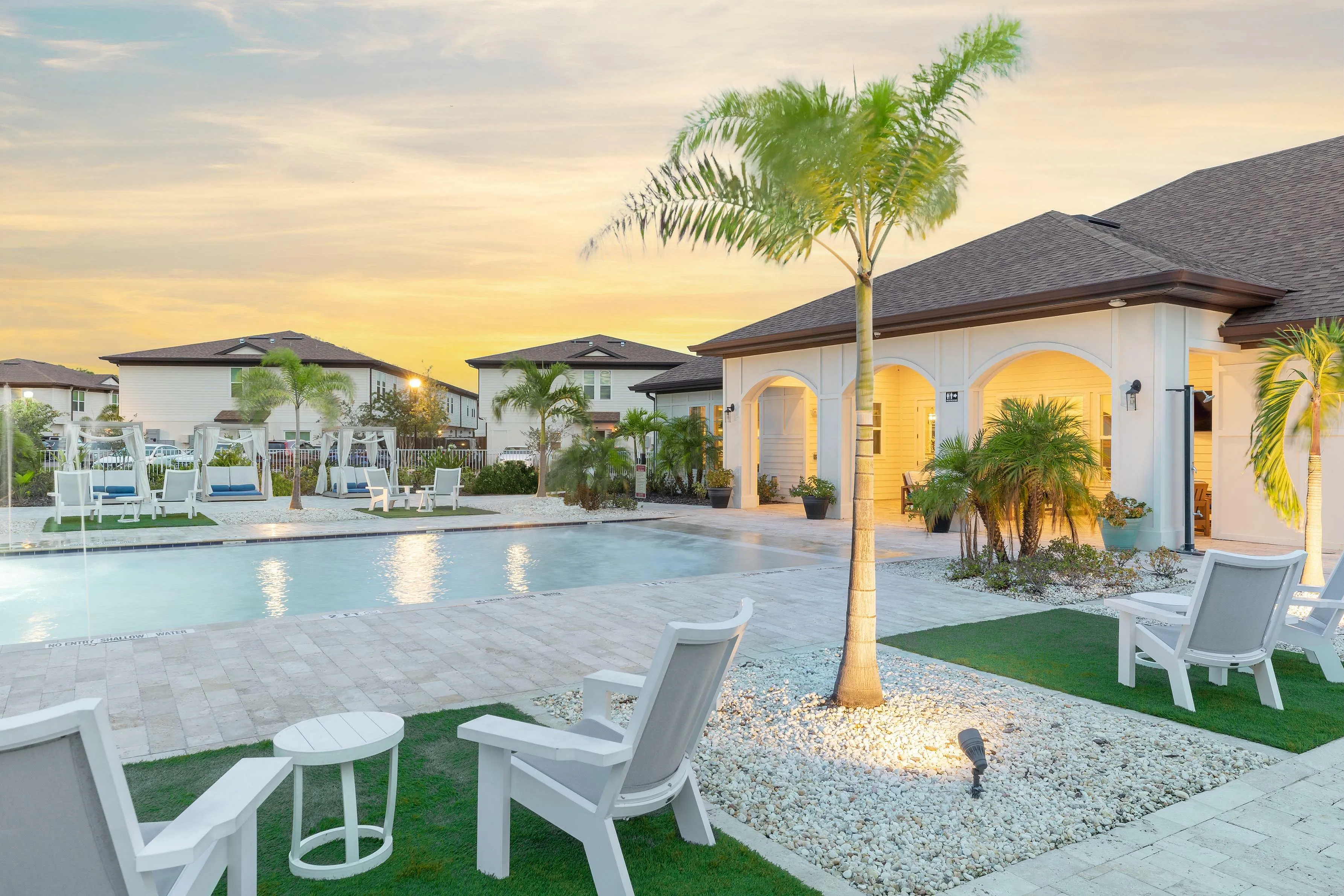Charming outdoor pool area with palm trees and lounge seating against a sunset backdrop.