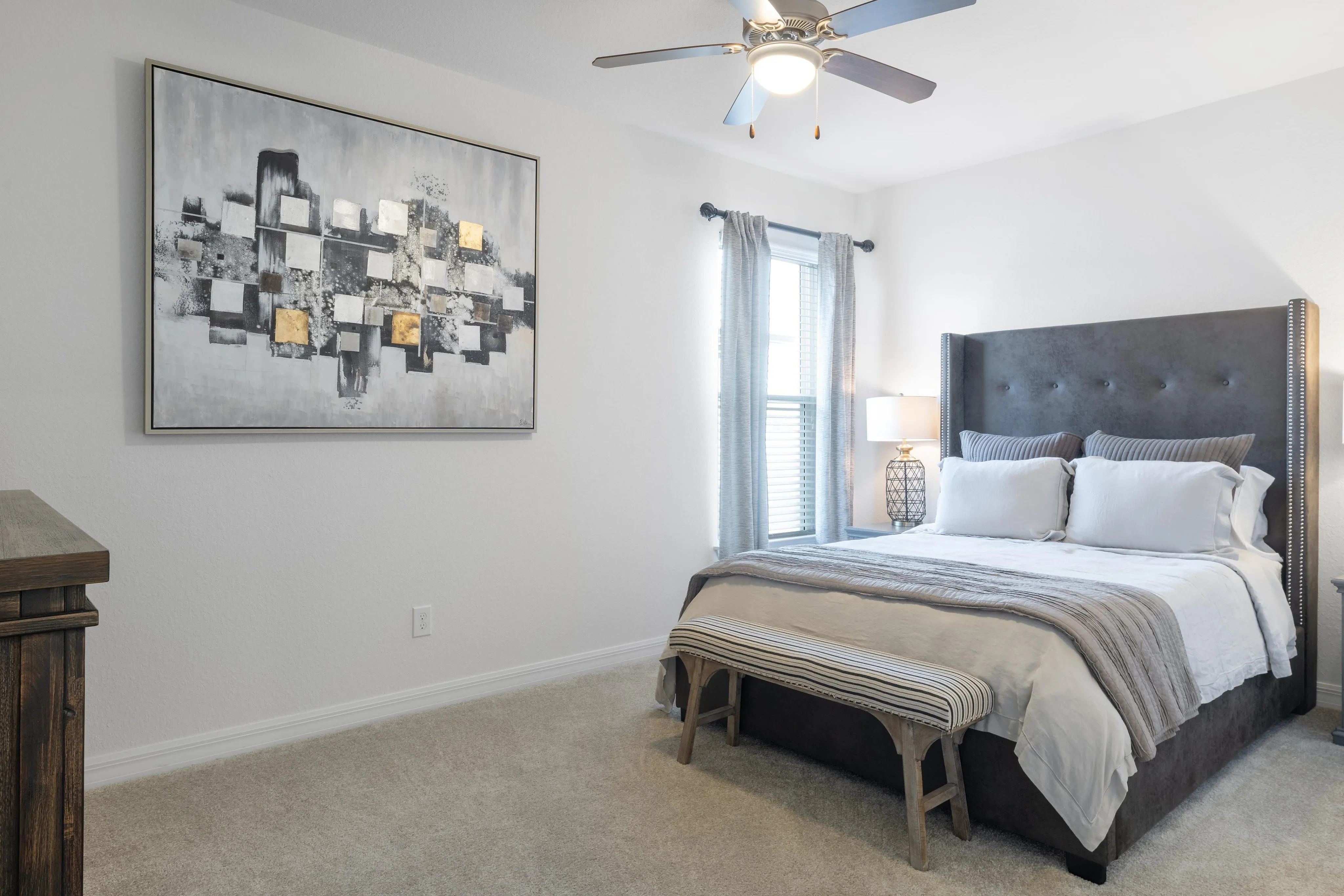 Tasteful bedroom with a plush grey bed, modern artwork on the wall, and soft natural lighting.