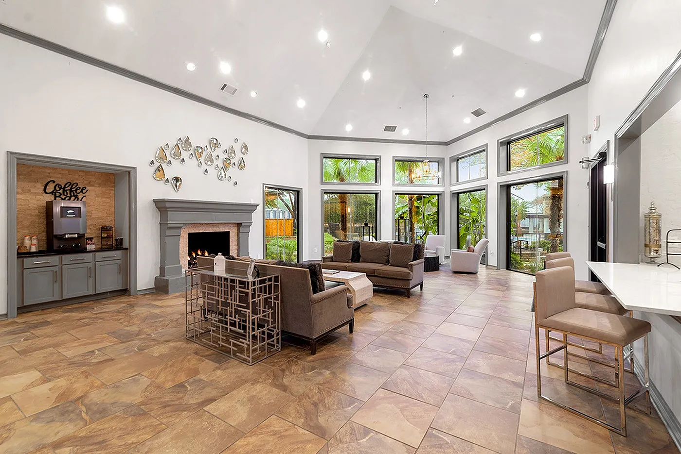 Inviting modern lounge area with elegant furnishings, cozy fireplace, and abundant natural light from large windows overlooking lush greenery.