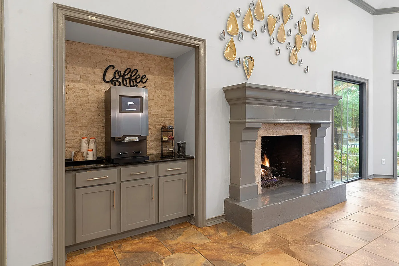 Inviting apartment space featuring a cozy fireplace, elegant gray cabinetry, and a convenient coffee station.