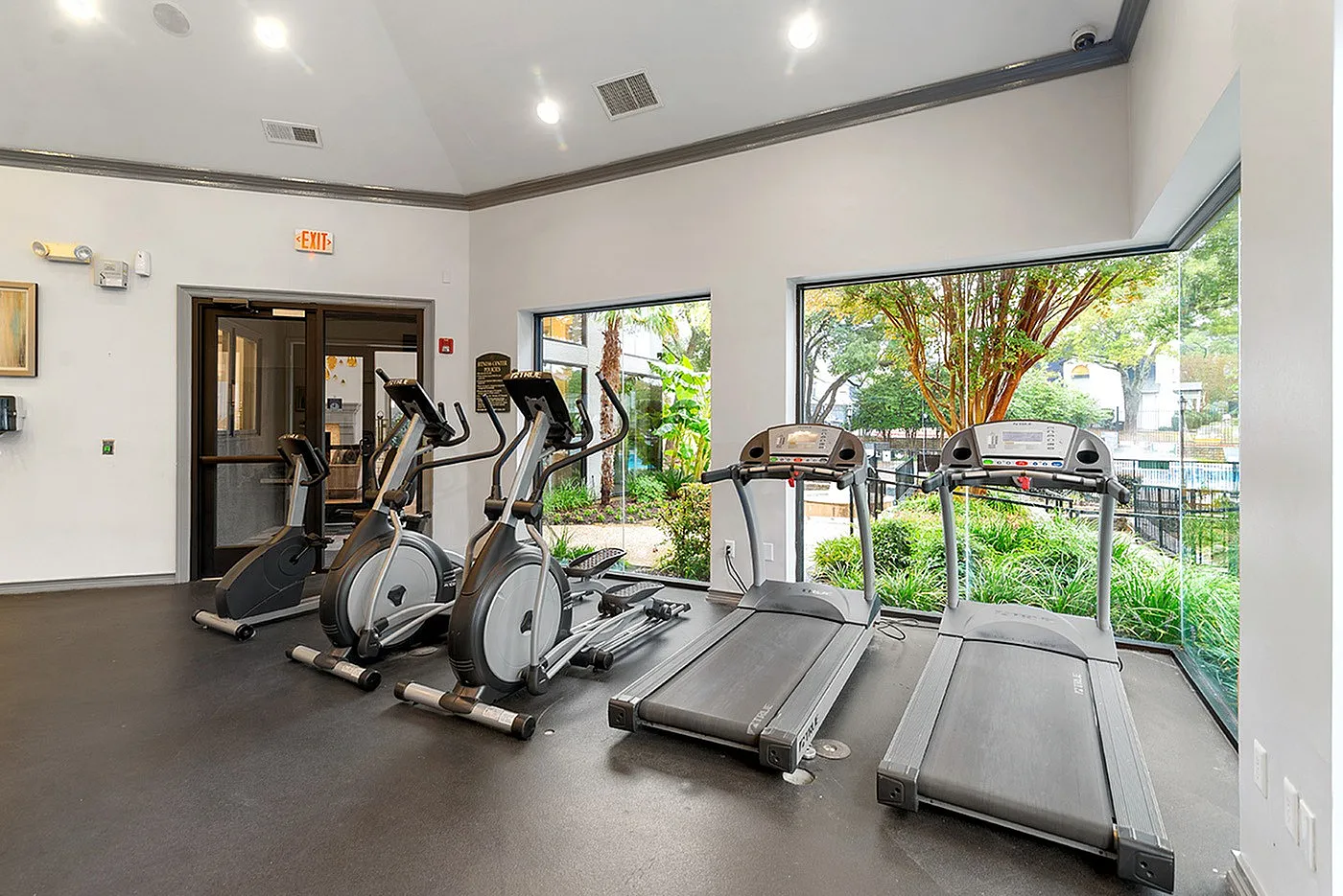 Bright and modern fitness center with cardio machines and large windows overlooking lush greenery.