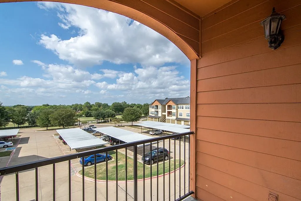 Inviting apartment balcony with a scenic view of manicured greenery and charming residential complexes under a vibrant blue sky.