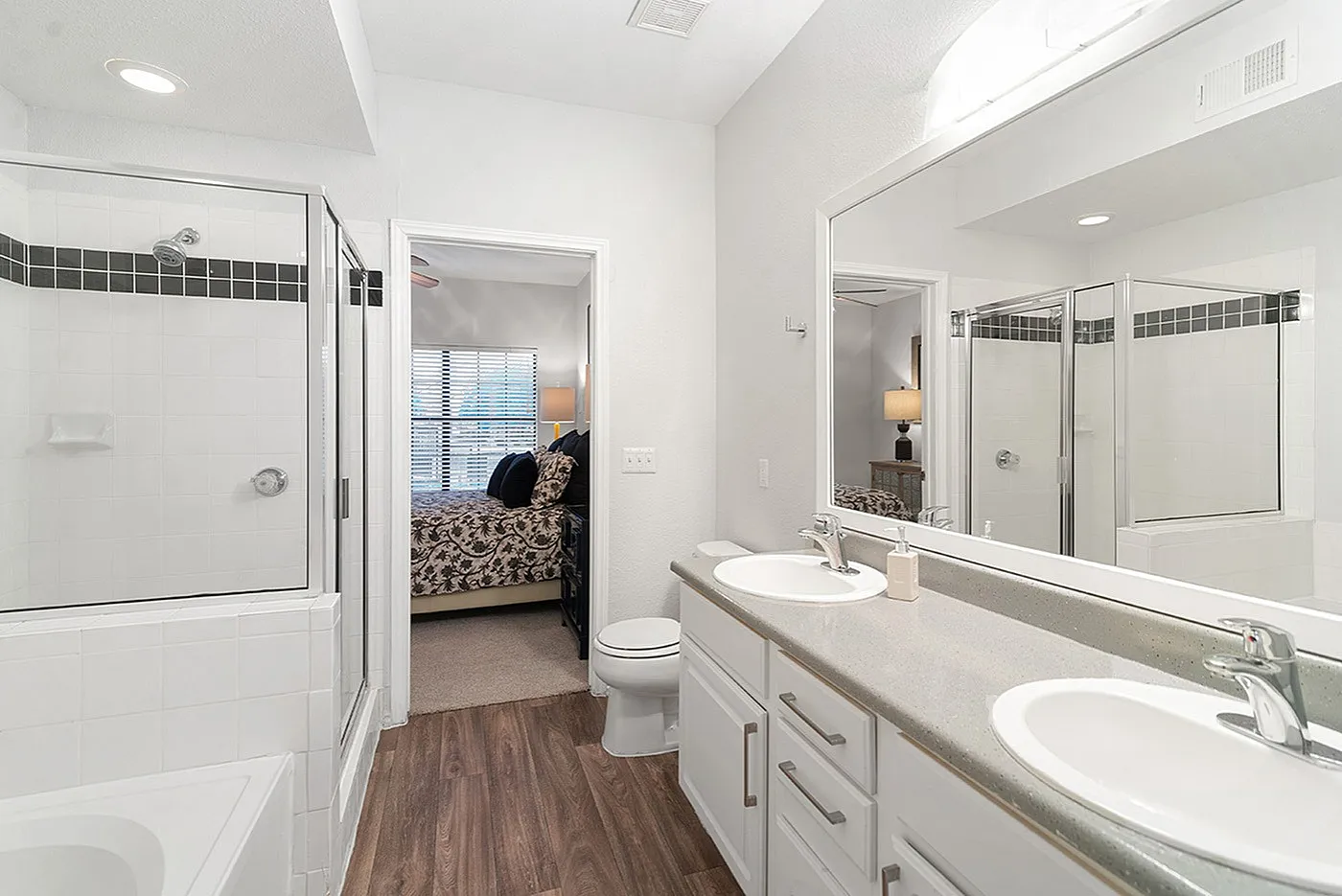 Modern bathroom with double sinks, spacious shower, and an inviting glimpse into a cozy bedroom.