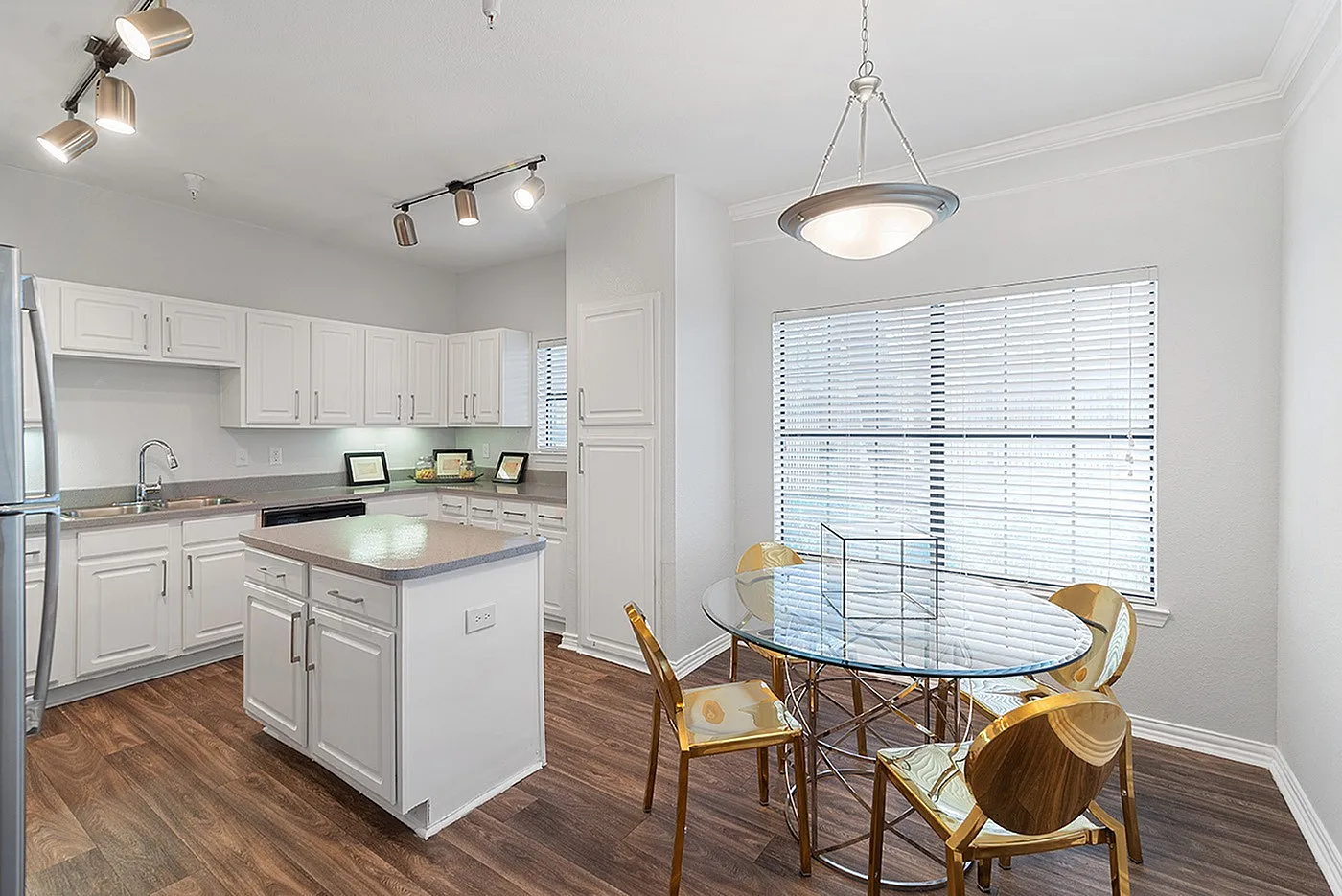Bright and modern kitchen with elegant white cabinets, sleek island, and chic dining area boasting golden chairs and a glass table.