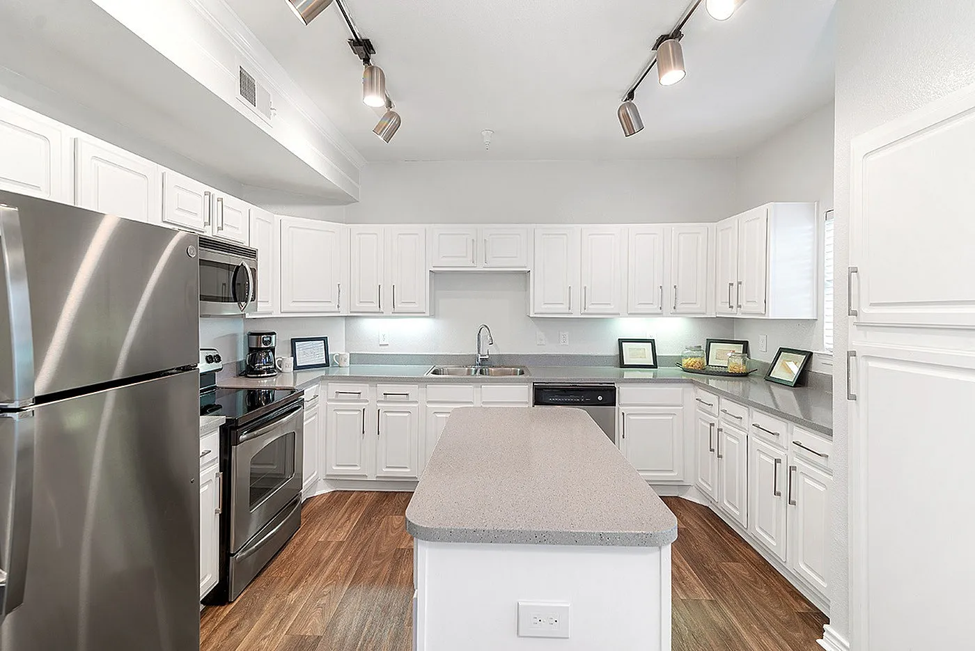 Modern kitchen with bright white cabinetry, sleek stainless steel appliances, and elegant overhead lighting.