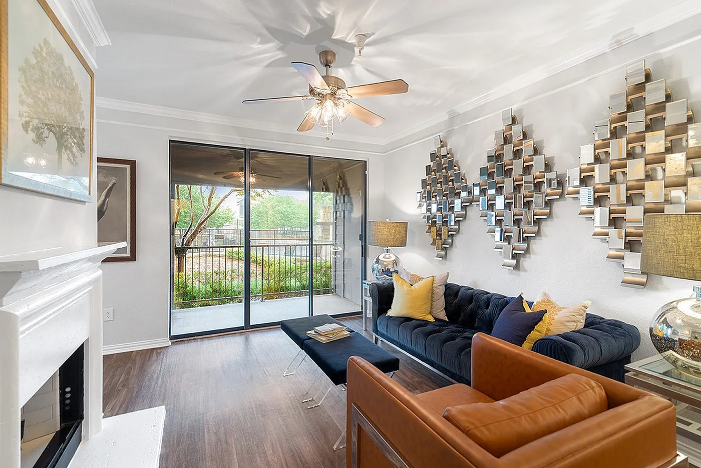 Elegant living room with chic decor, featuring a plush navy sofa, stylish metal wall art, and a large sliding glass door leading to a lush outdoor view.