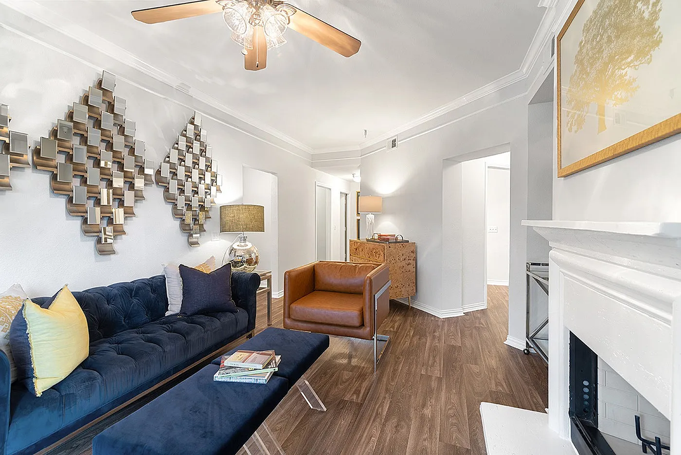 Chic living room with modern decor, featuring a navy velvet sofa, stylish armchair, and elegant geometric wall art under a ceiling fan.
