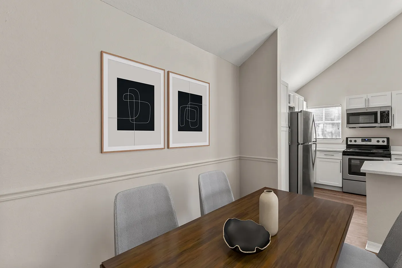Chic dining area with modern art, sleek furniture, and a view into a contemporary kitchen featuring stainless steel appliances.