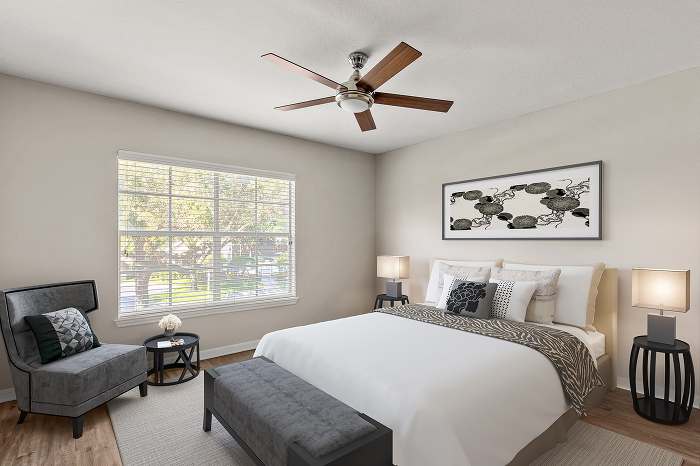 Bright and modern bedroom with elegant decor, featuring a stylish ceiling fan, cozy seating nook by a large window, and tasteful artwork on the wall.