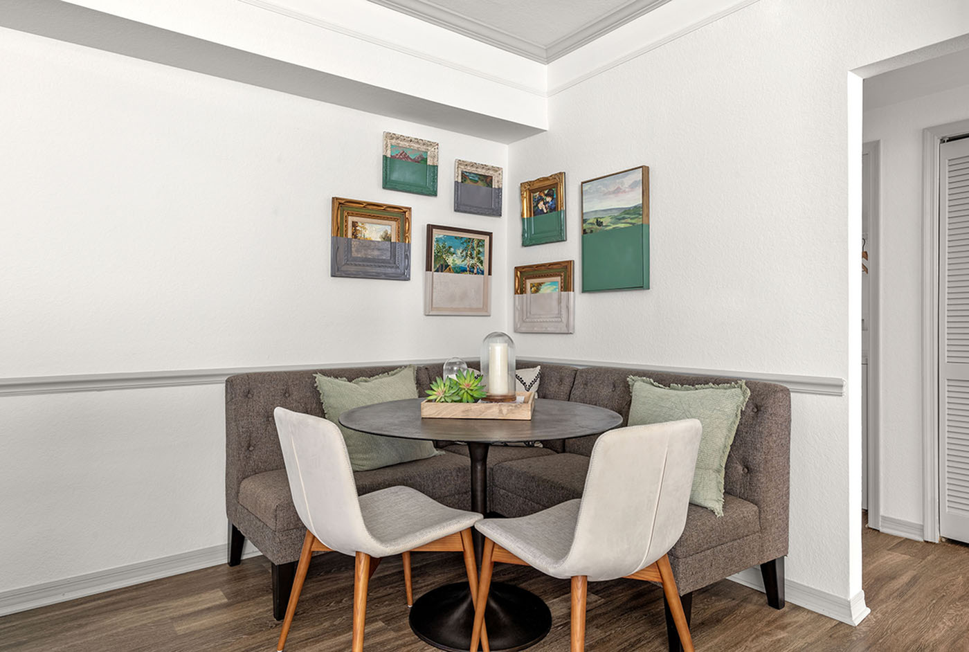 Charming dining nook with a cozy corner bench, stylish round table, and modern chairs, adorned with contemporary art on white walls.