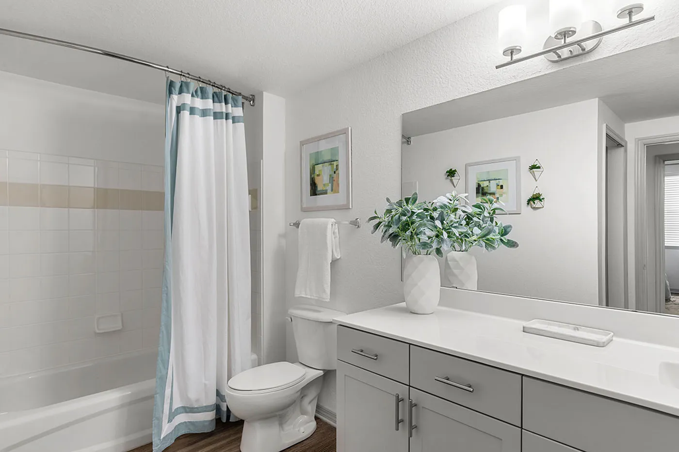 Inviting modern bathroom featuring a sleek vanity, chic lighting, and a stylish shower curtain. Fresh and elegant design with decorative greenery for a serene atmosphere.