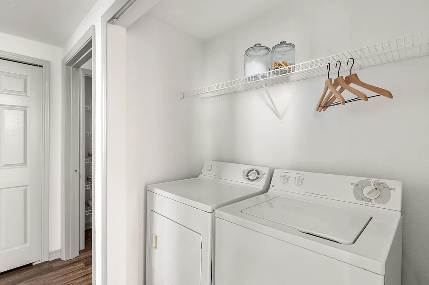 Compact and convenient laundry room with modern washer and dryer, featuring elegant shelving and wooden hangers for organized living.