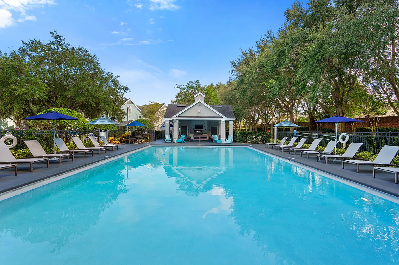 Inviting outdoor pool area with luxurious sun loungers and vibrant umbrellas, surrounded by lush greenery and a charming pool house.