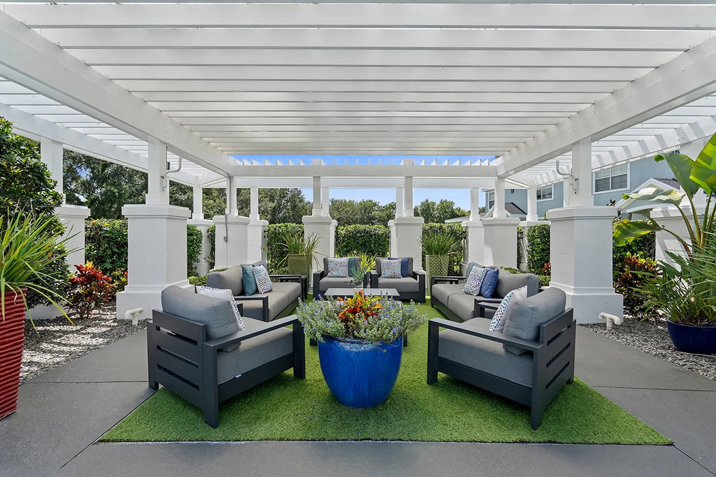 Chic outdoor patio featuring plush seating under a stylish white pergola, surrounded by lush greenery and vibrant potted plants.
