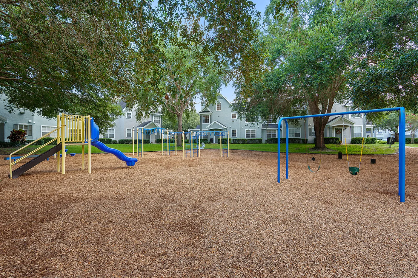 Charming playground with vibrant slides and swings, nestled under lush trees in a serene residential community.