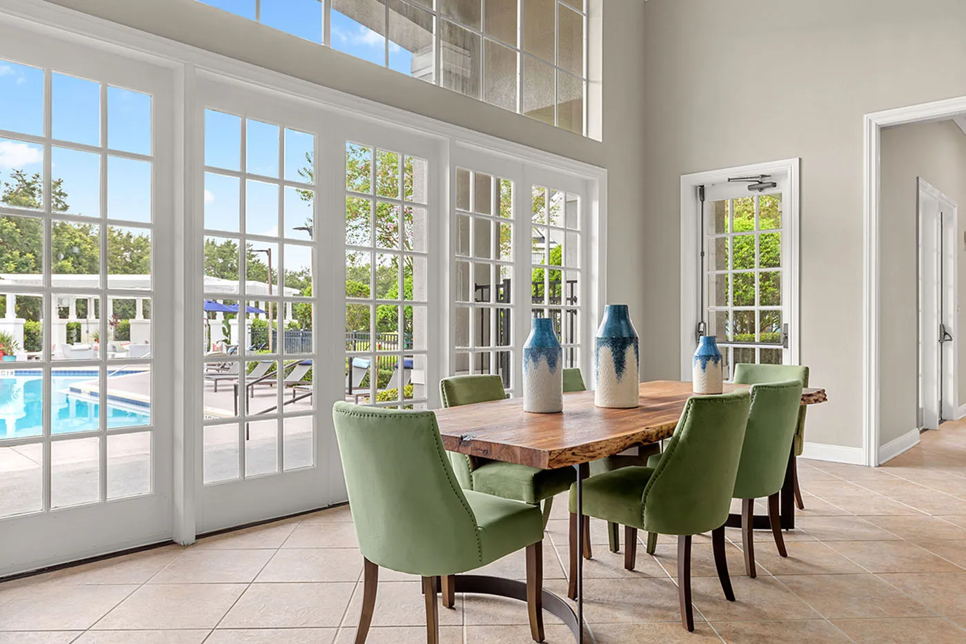 Bright dining area with green chairs and wooden table, overlooking a sparkling pool through elegant French doors.