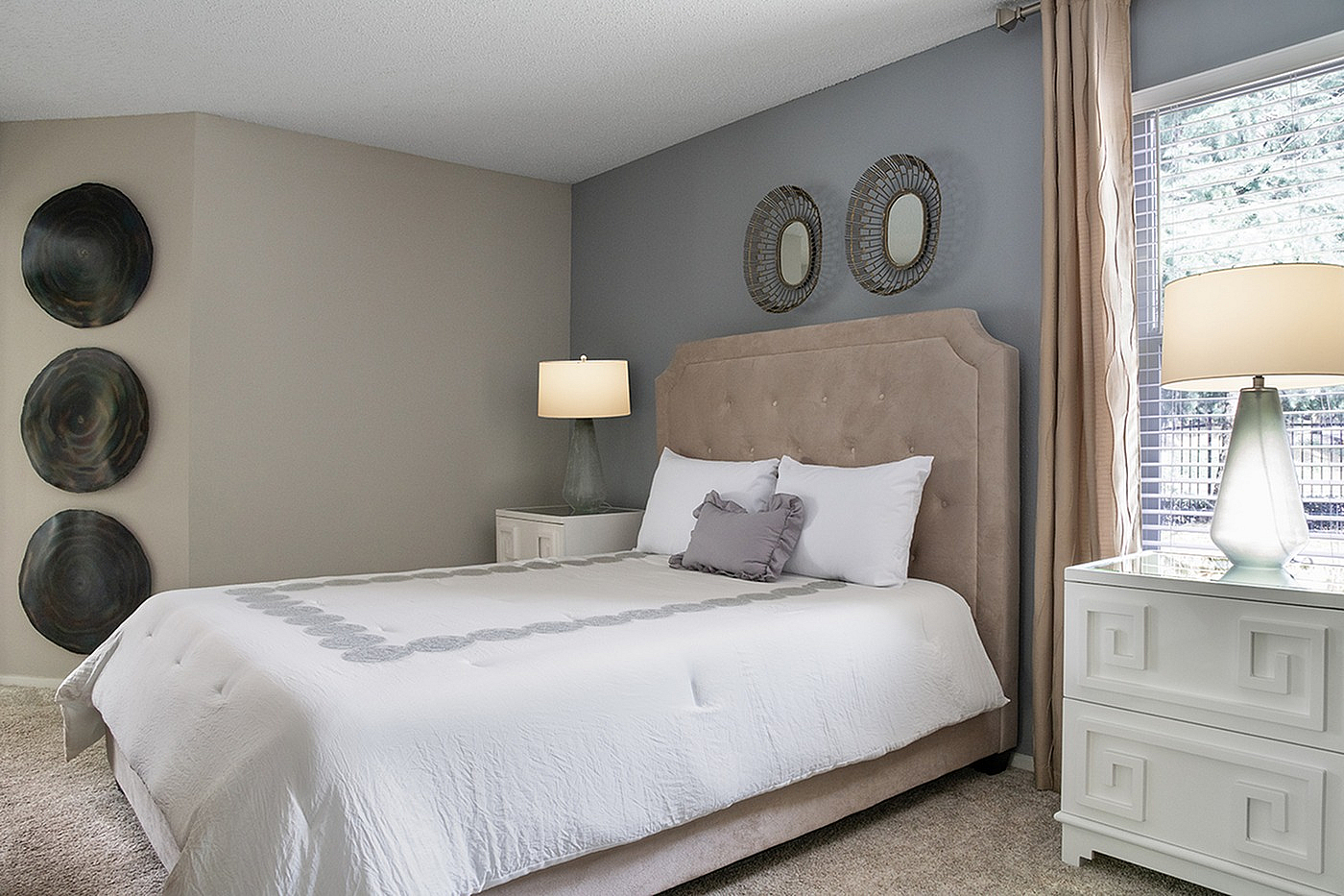 Elegant bedroom with plush upholstered bed, chic wall art, and stylish bedside tables illuminated by soft lamps.