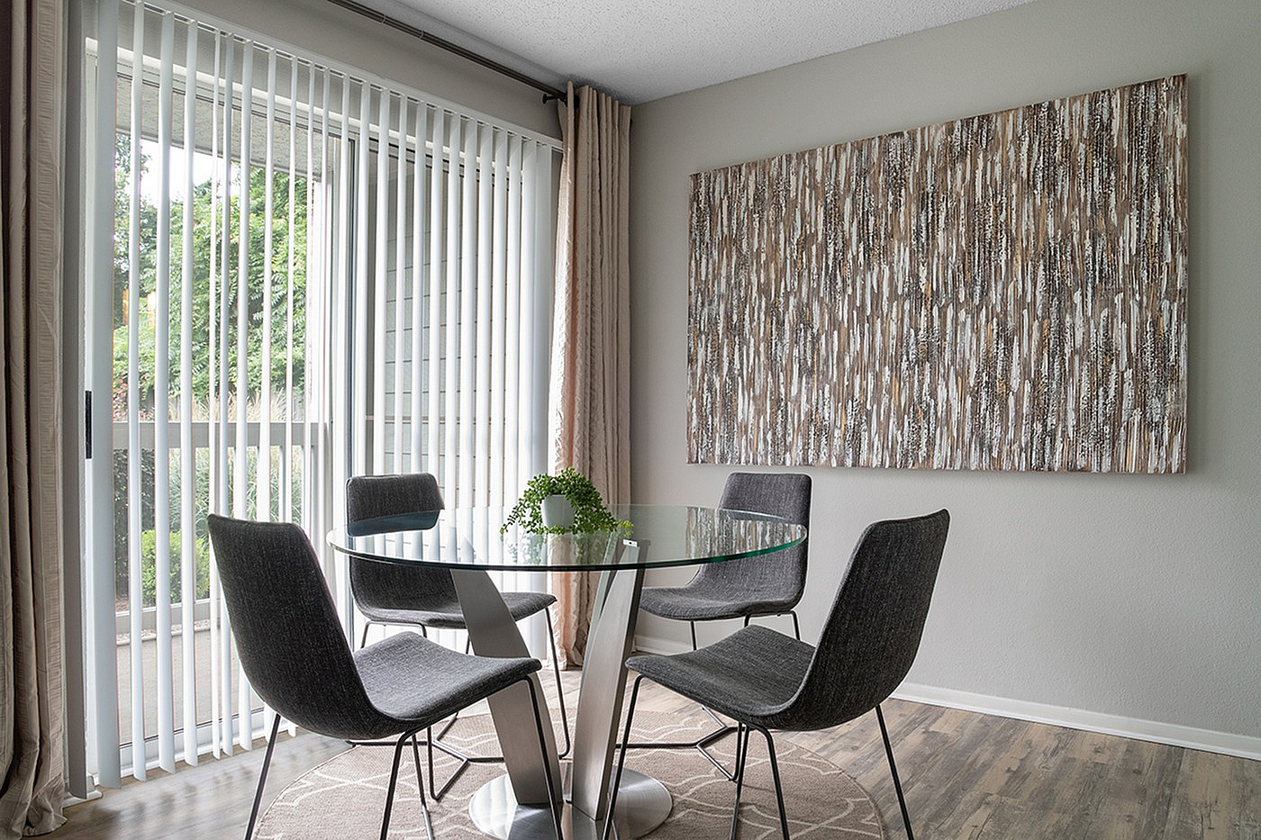 Contemporary dining area with glass table, modern chairs, and floor-to-ceiling windows offering garden views.