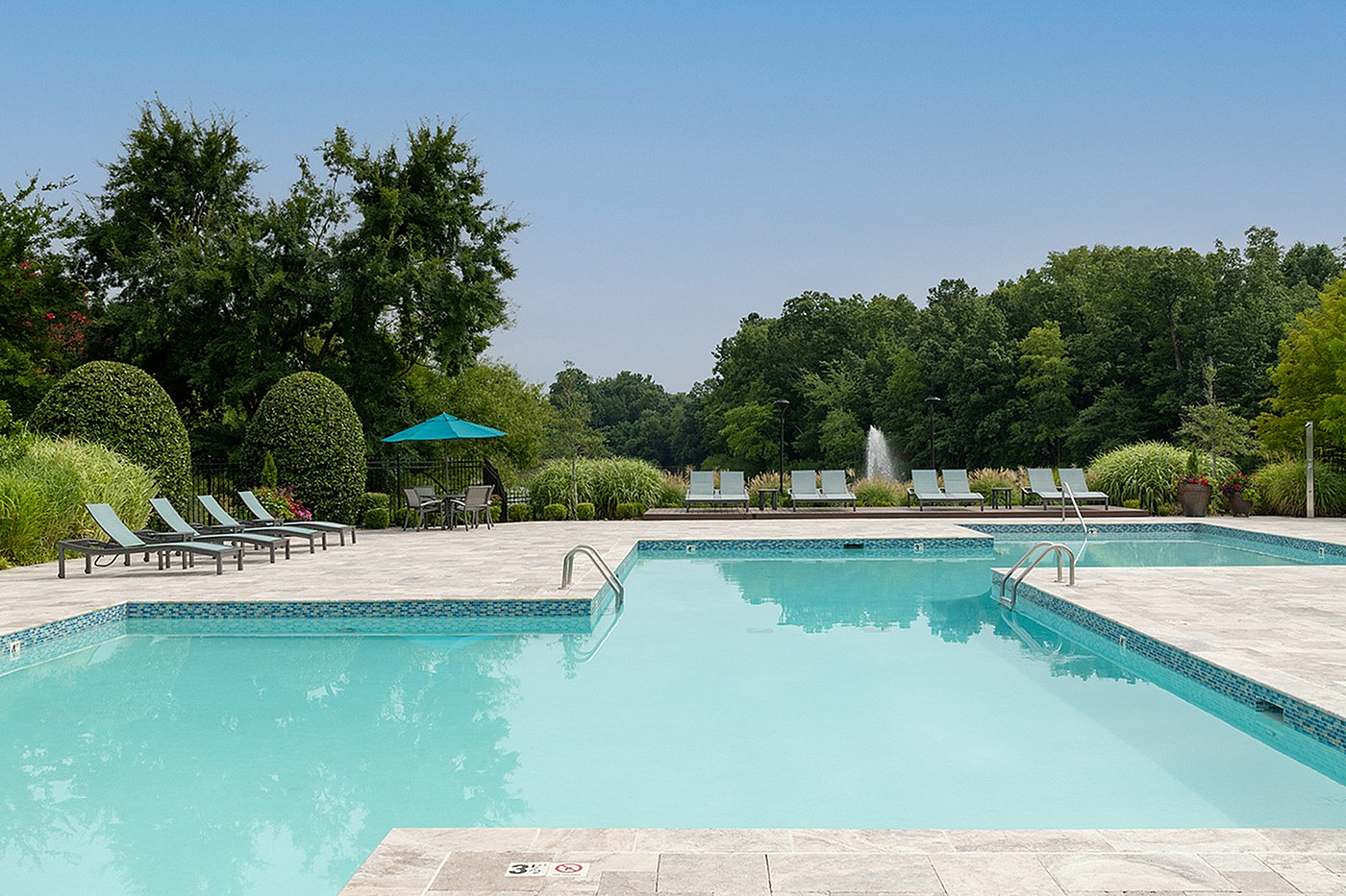 Inviting outdoor swimming pool with surrounding lounge chairs and lush greenery, offering a serene and relaxing atmosphere.