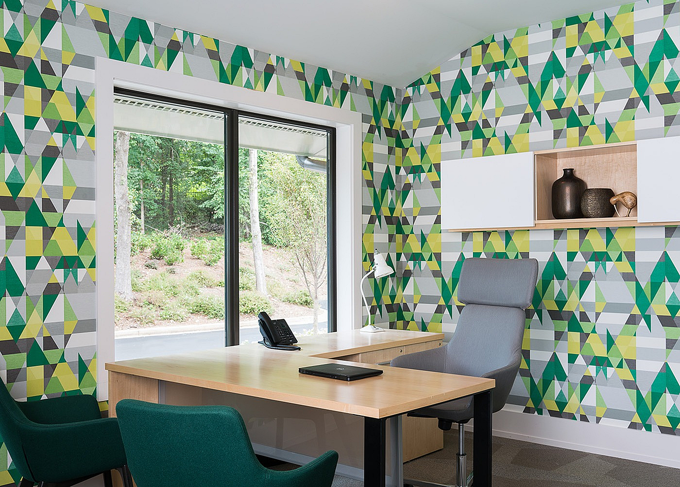 Modern office space with vibrant geometric wall design, large window view, wooden desk, and stylish chairs.